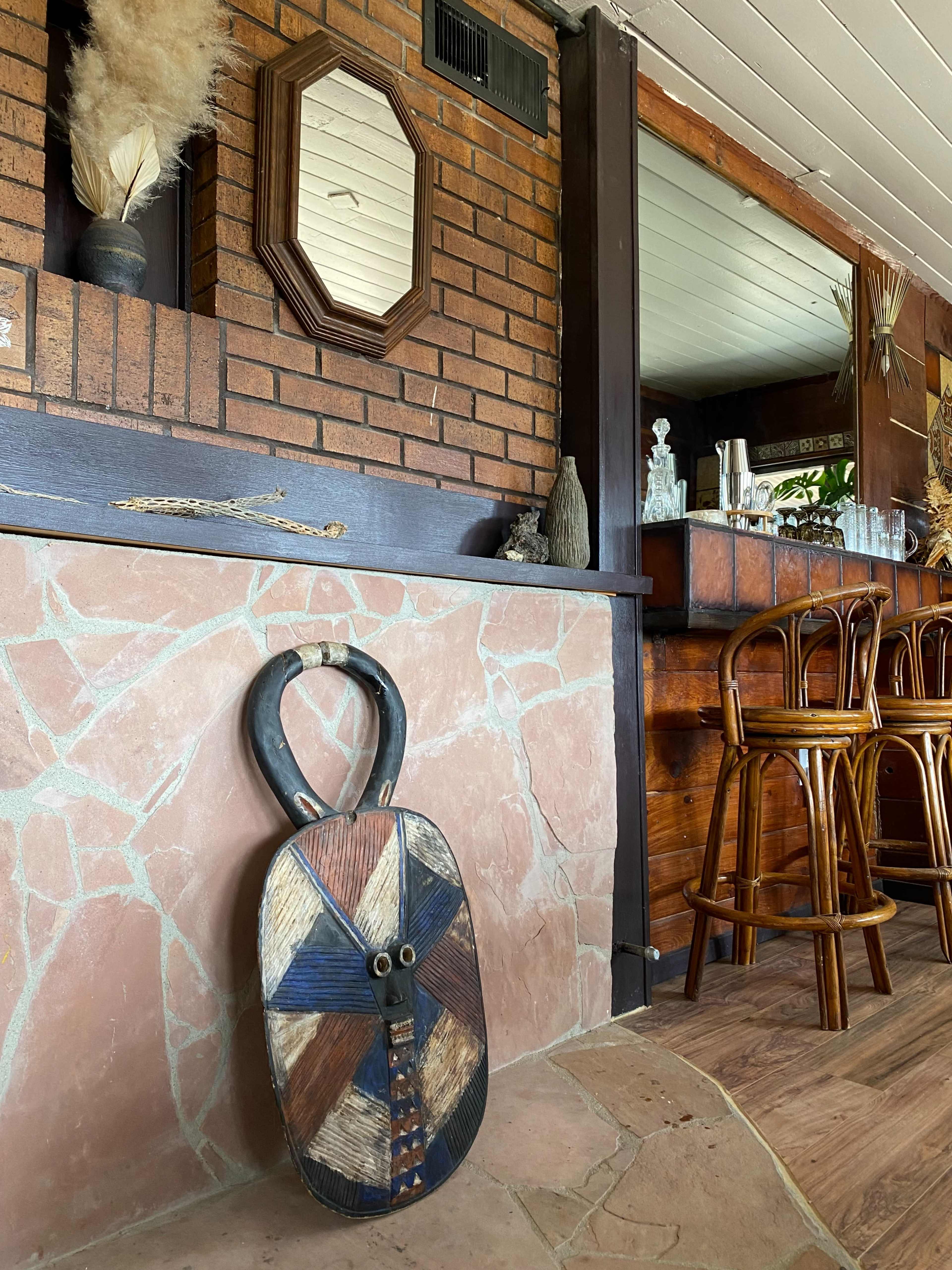 A decorative wooden shield leans against a stone wall beside a bar with bar stools in a rustic interior.