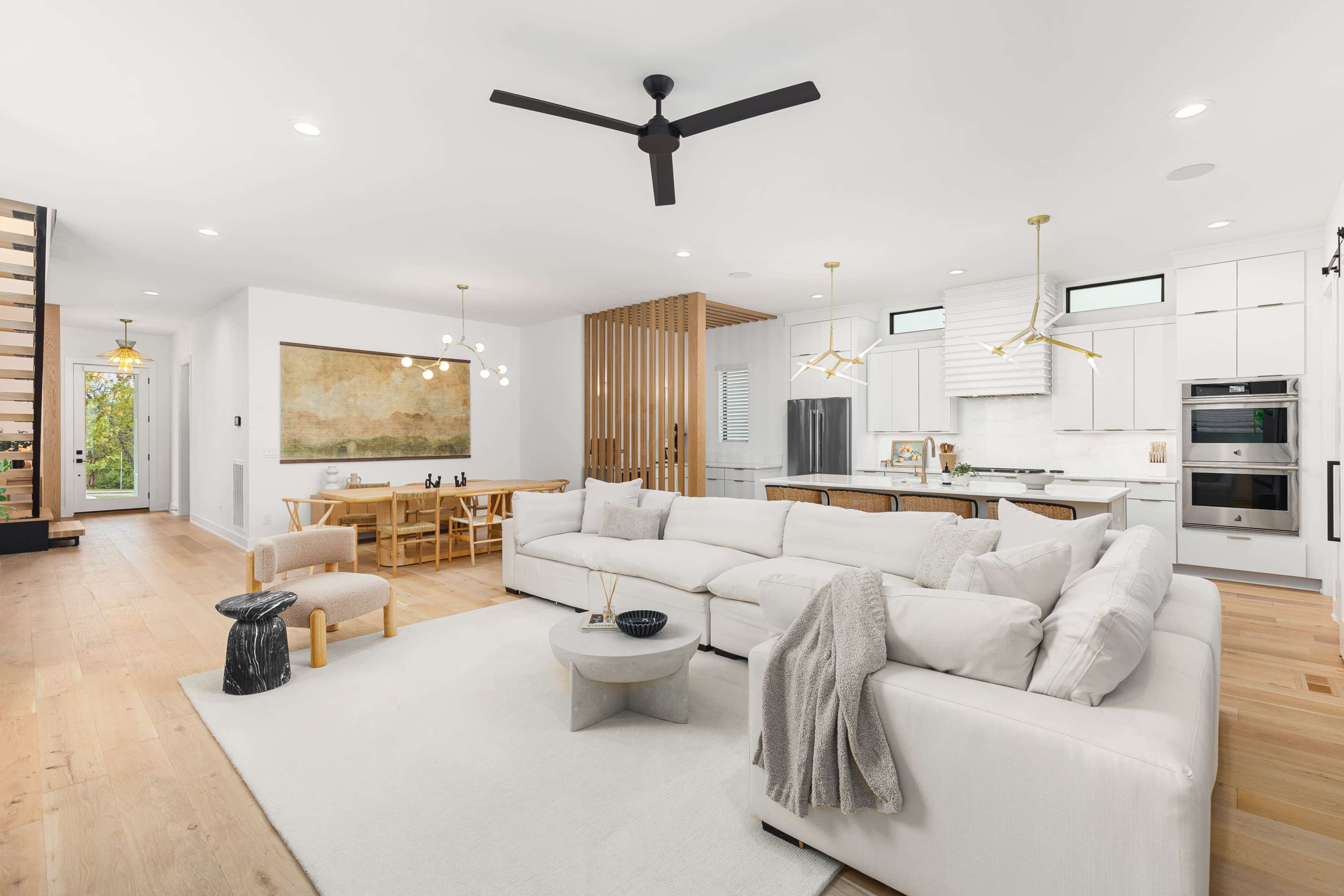 The image shows a modern living room and dining area featuring a large sectional sofa, a sleek dining table, and a mix of wood and white cabinetry.