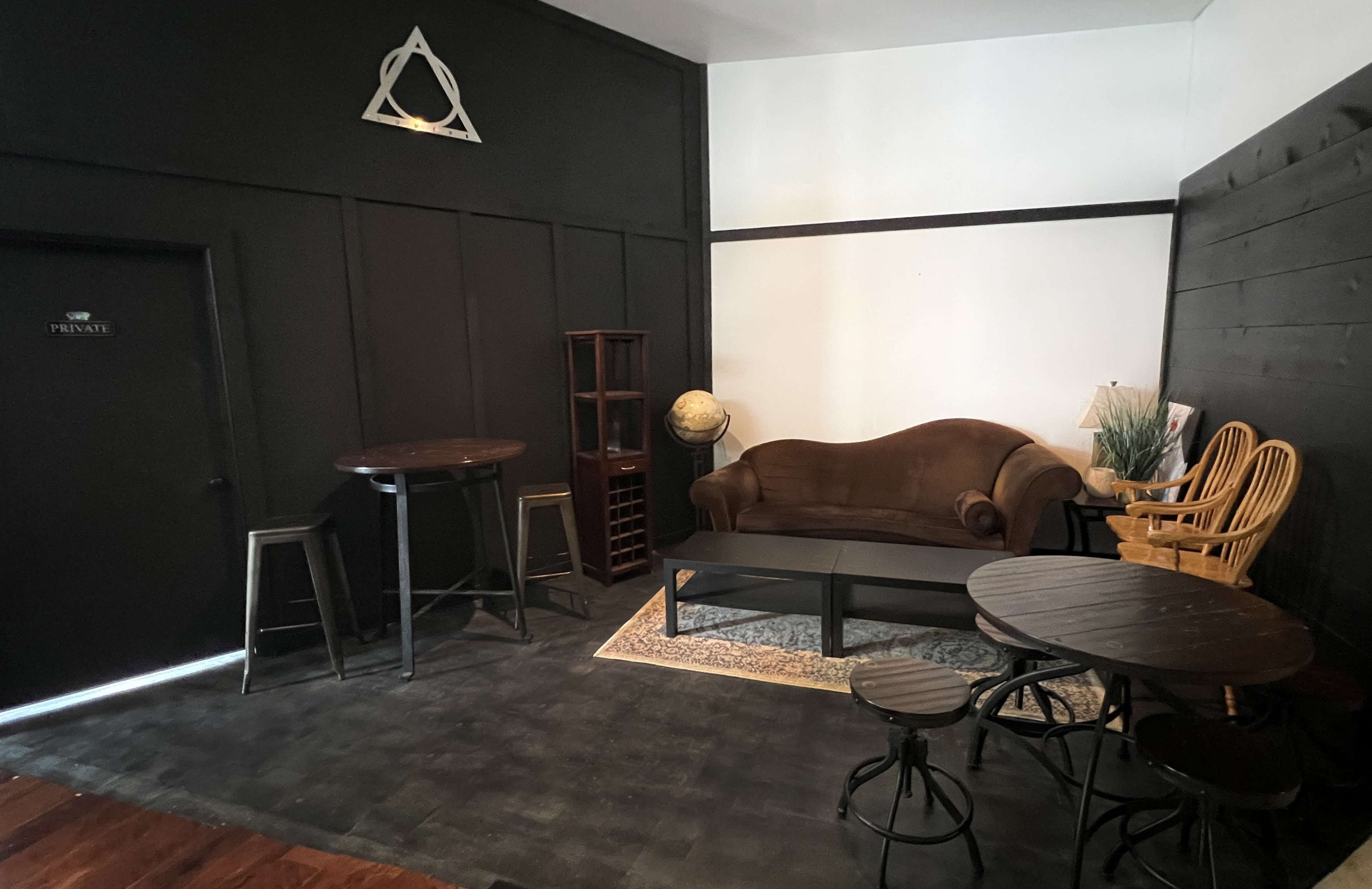 A small, darkly painted room with a brown couch, a globe on a shelf, and multiple tables and chairs arranged around the space.