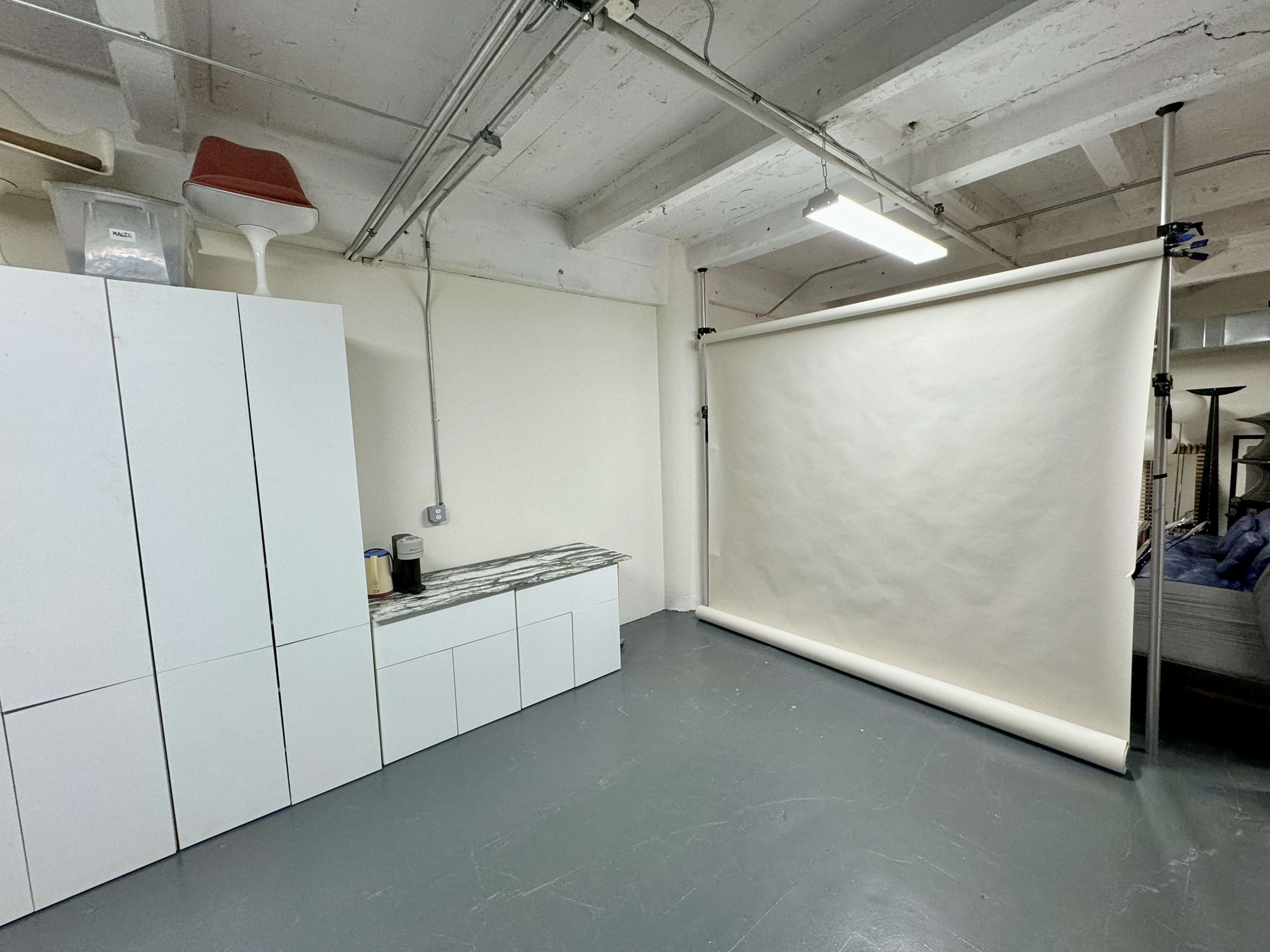 A minimalist studio space featuring a roll of plain backdrop paper against a wall, a cabinet with a countertop, and a few decorative items on shelves above.