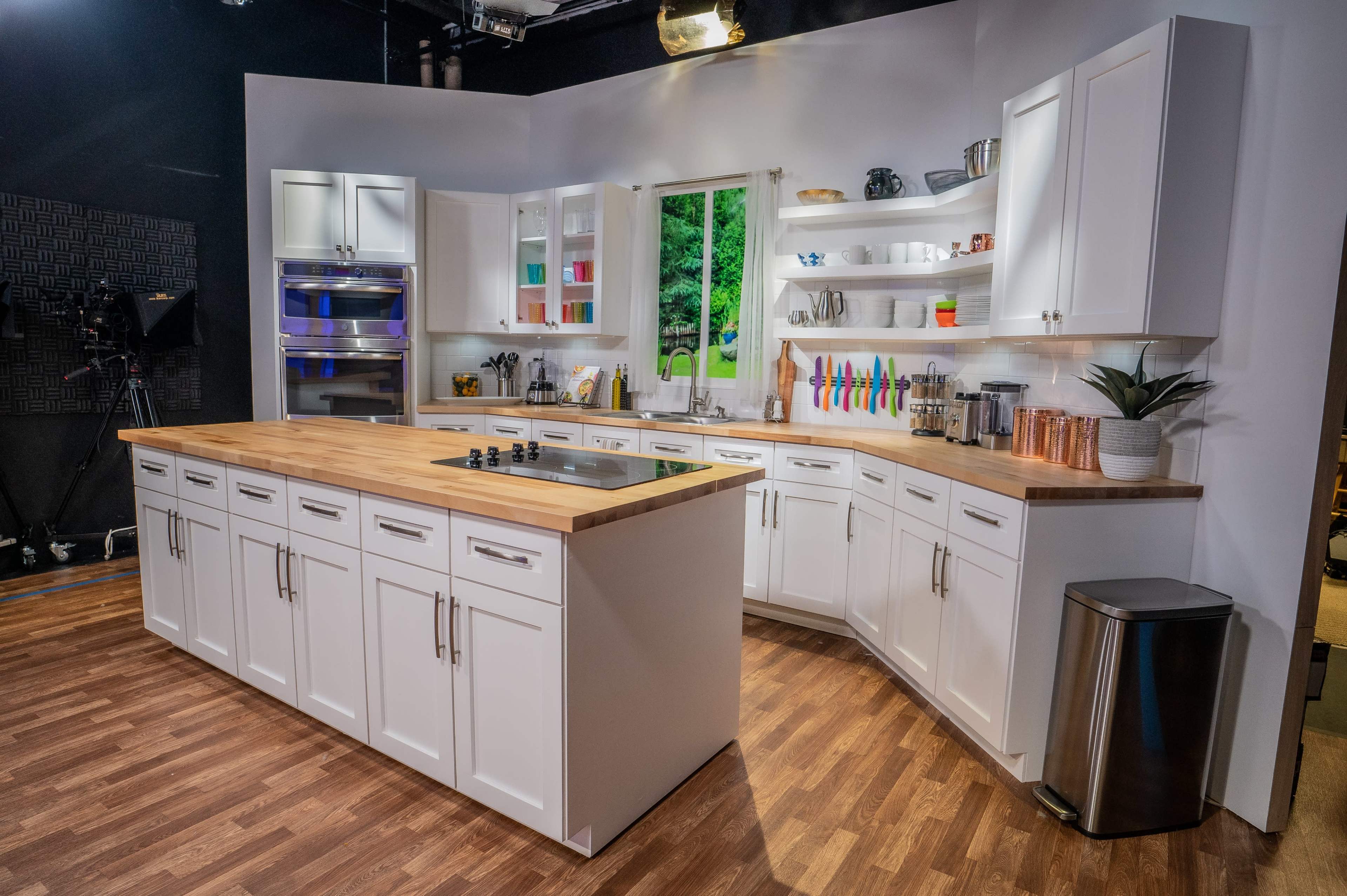 A modern kitchen is shown with white cabinetry, a wooden countertop, and large windows overlooking a green landscape.