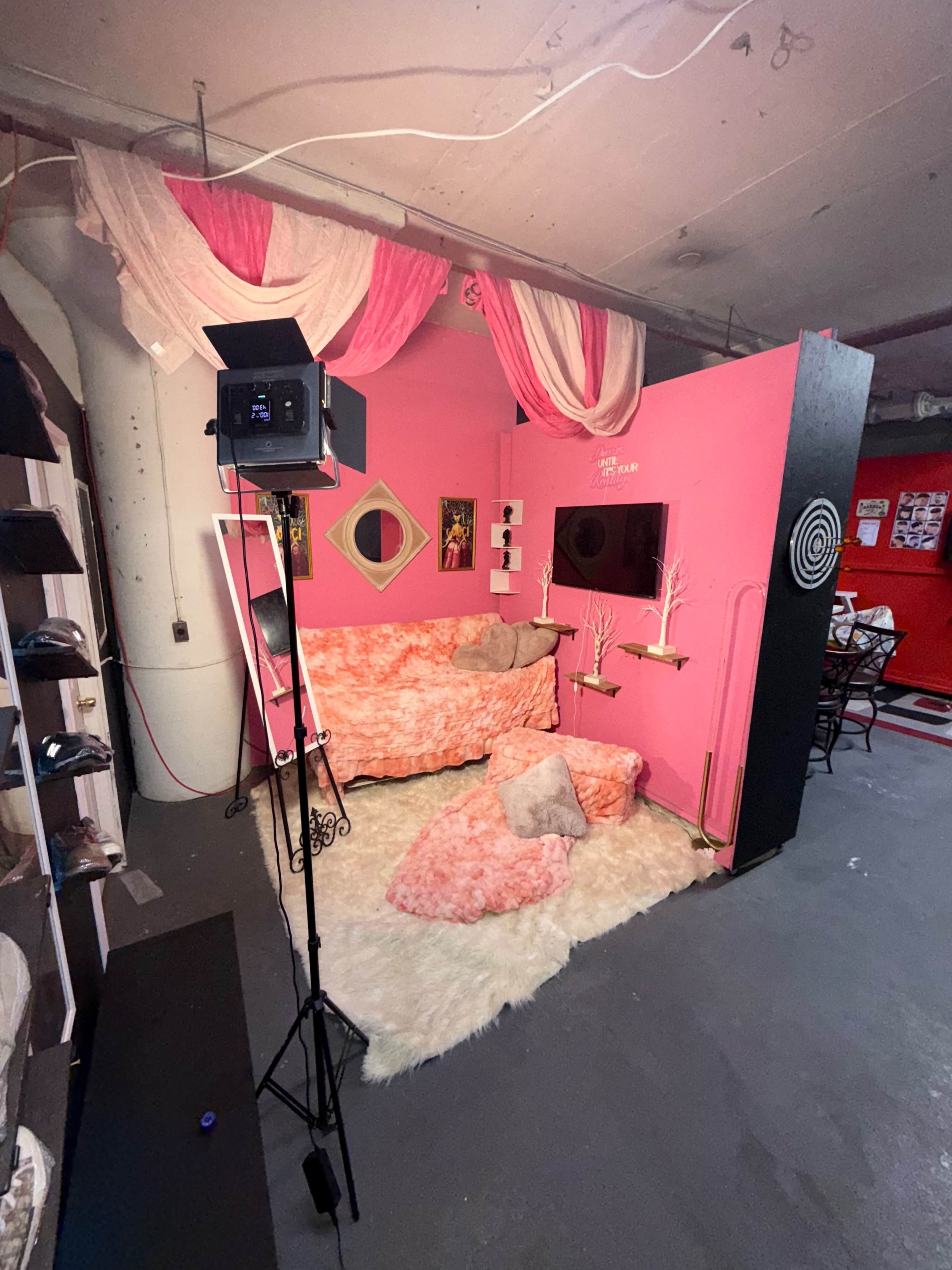 The image shows a brightly colored pink room with a couch, decorative elements, and a soft rug, illuminated by a standing light.