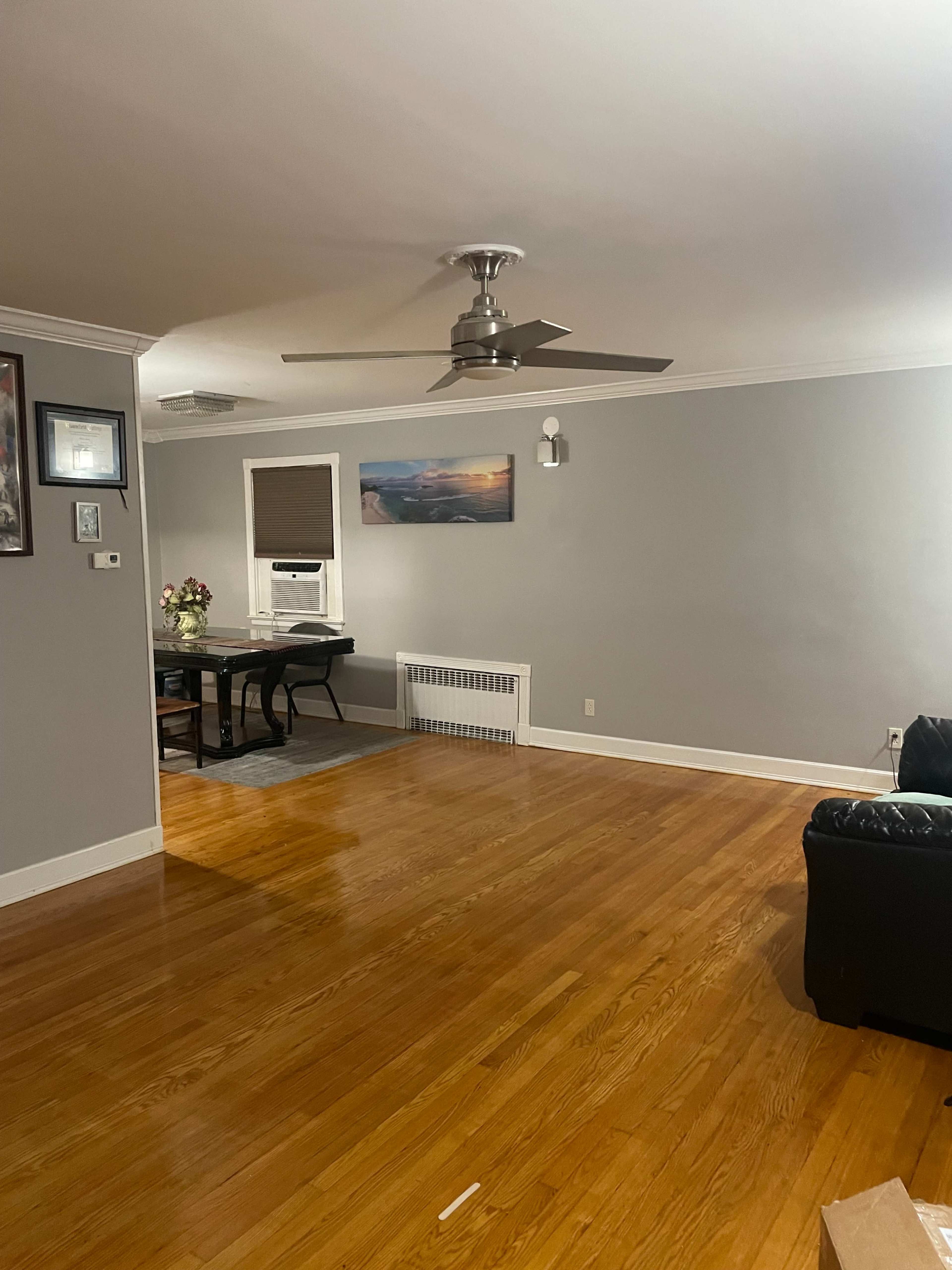 The image depicts a living room with hardwood floors, a dining table, a ceiling fan, and a window with blinds.