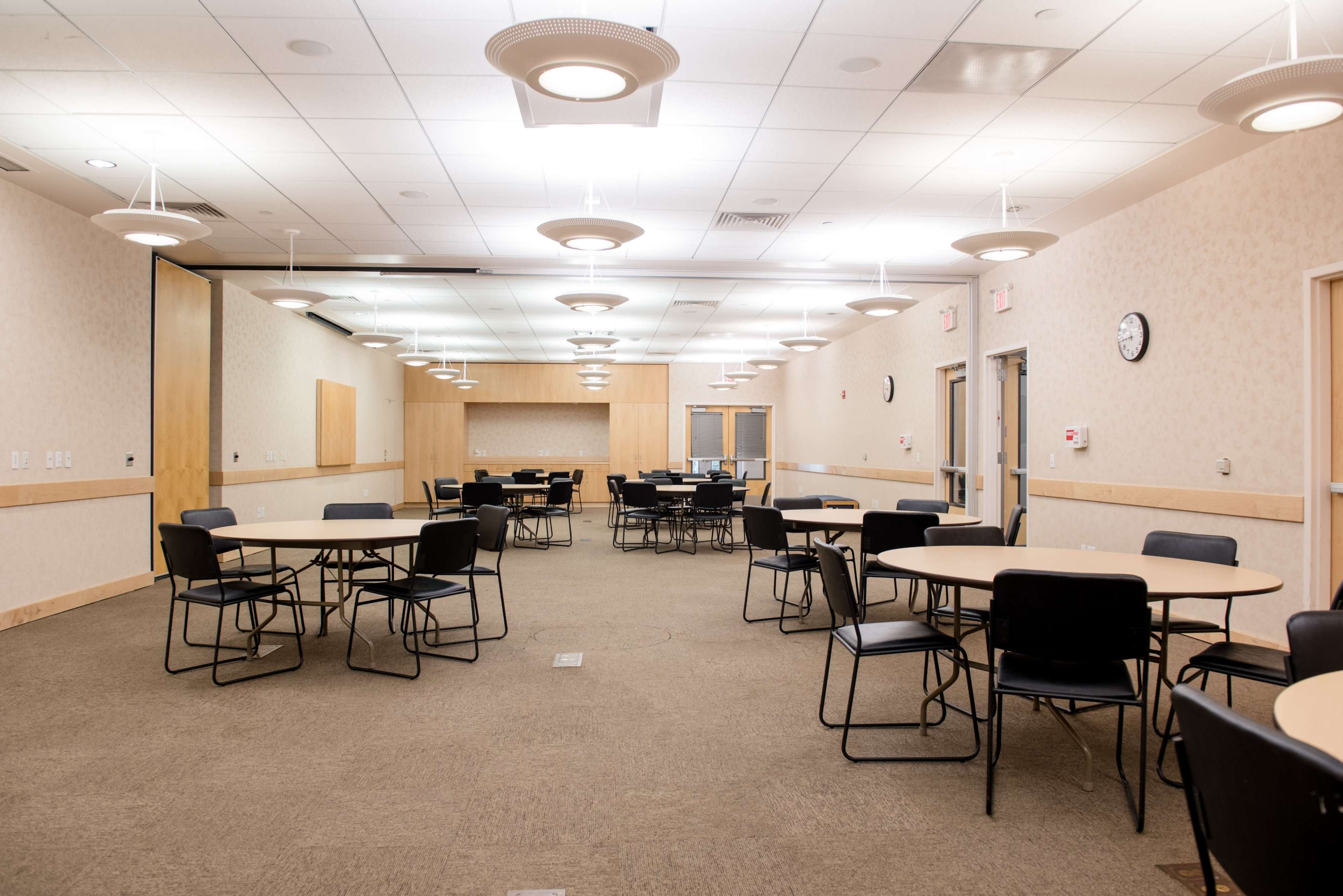 A large, empty meeting room with circular tables and black chairs arranged throughout the space.