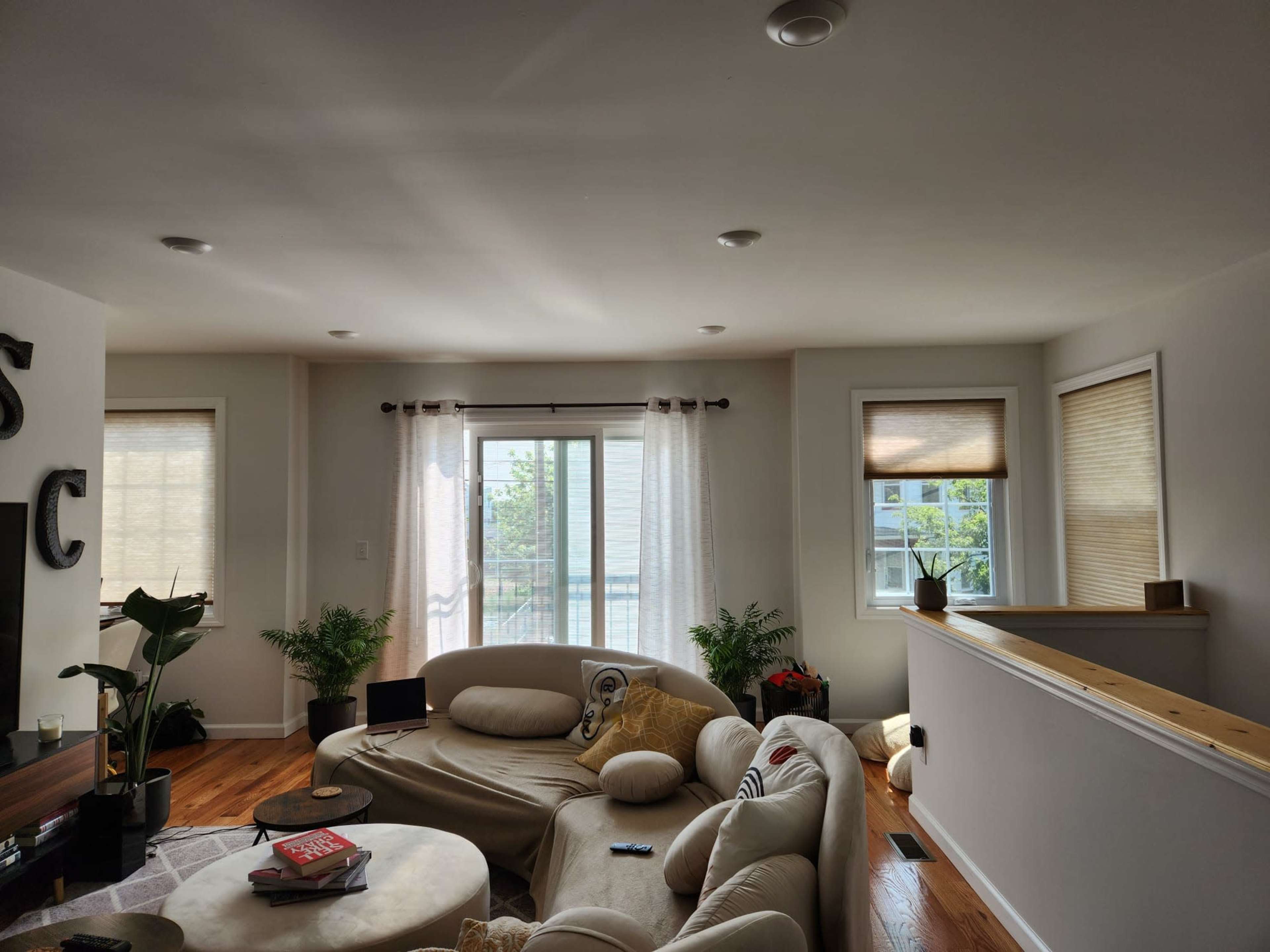 A bright living room with a circular sofa, wooden floors, and large windows covered with sheer curtains.