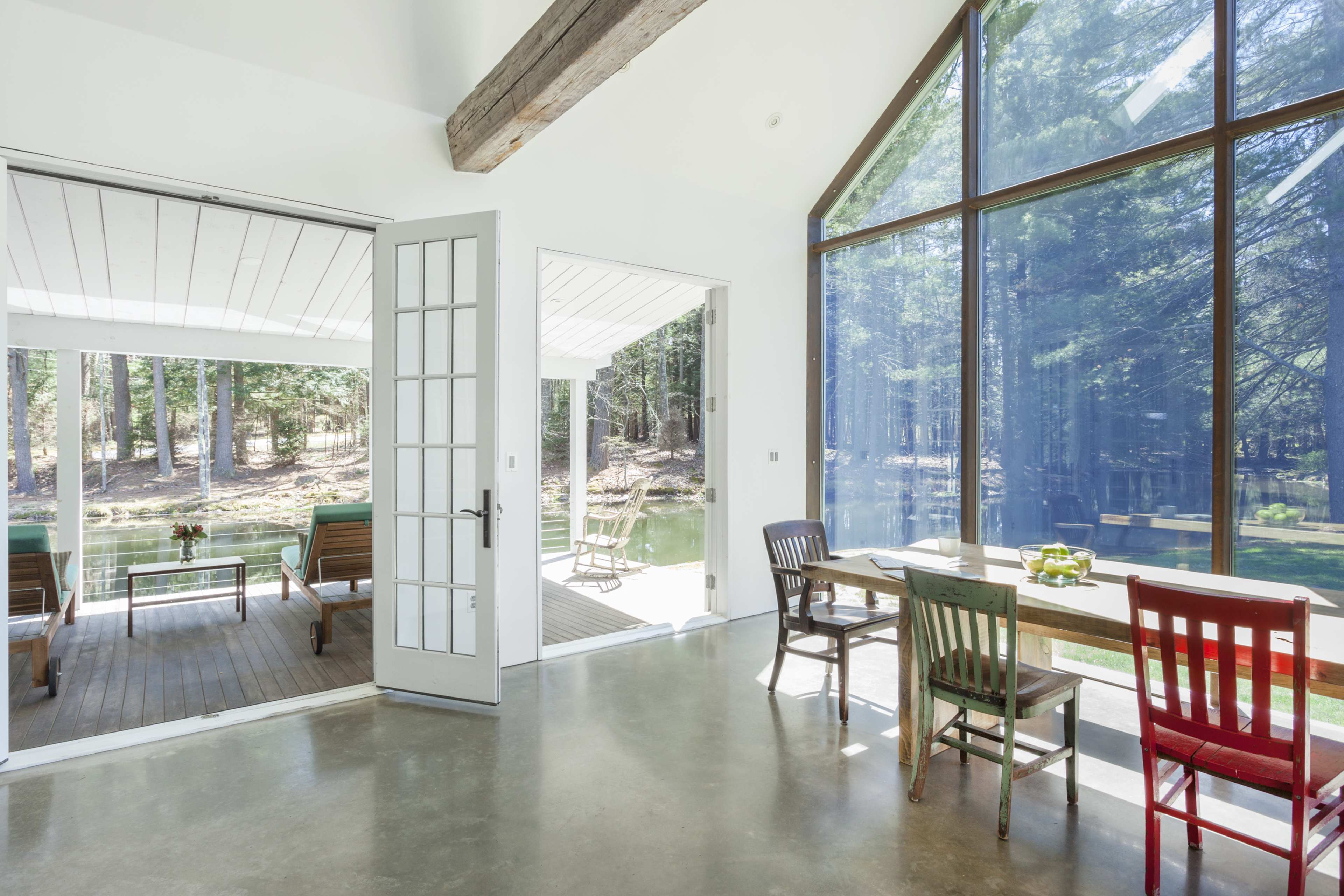 A modern interior space with large windows overlooking a forest, featuring a dining table and chairs, along with a door leading to an outdoor area.