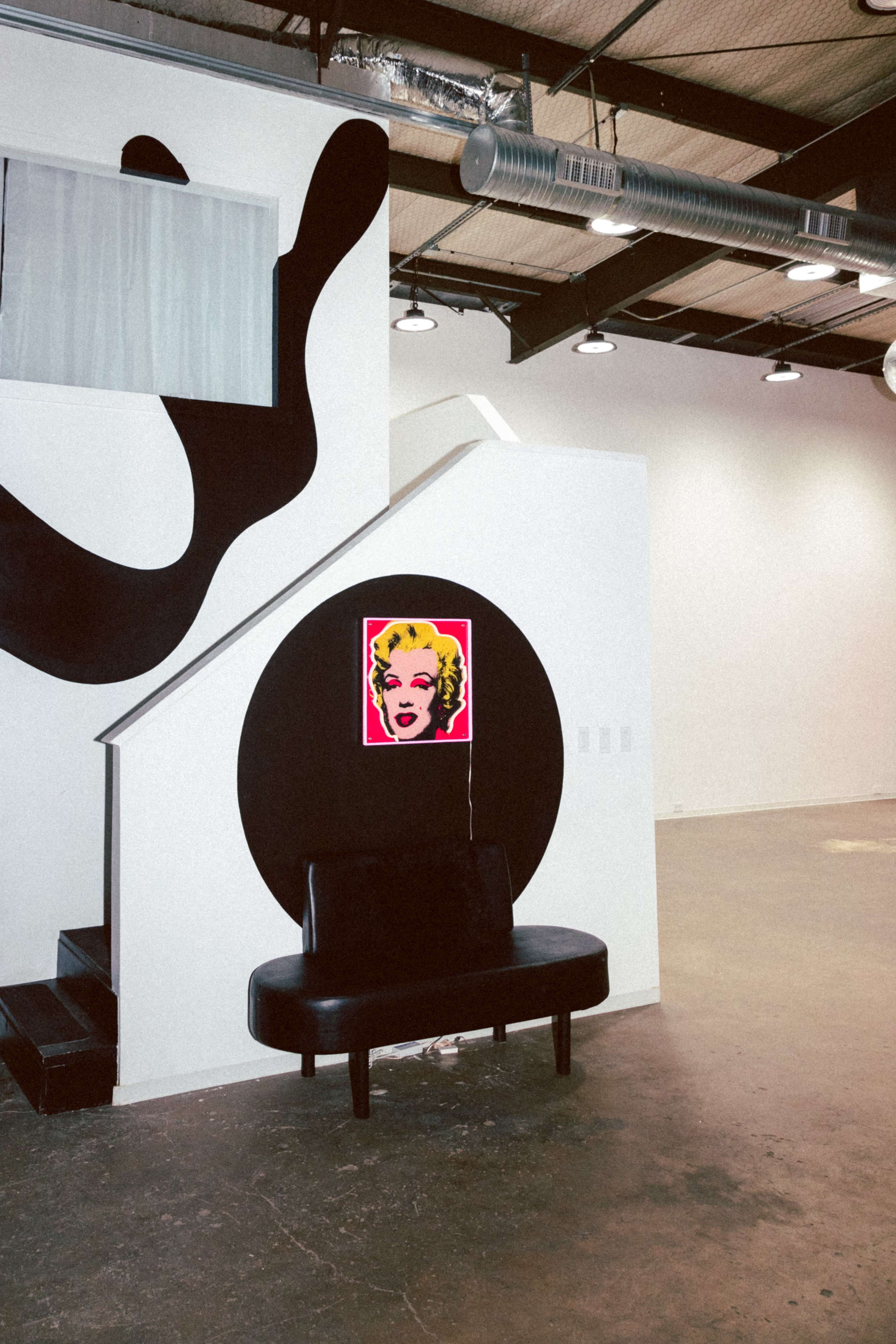 A black bench sits against a wall featuring a large round design and a colorful artwork of a woman above it, while a staircase leads to another level in the background.
