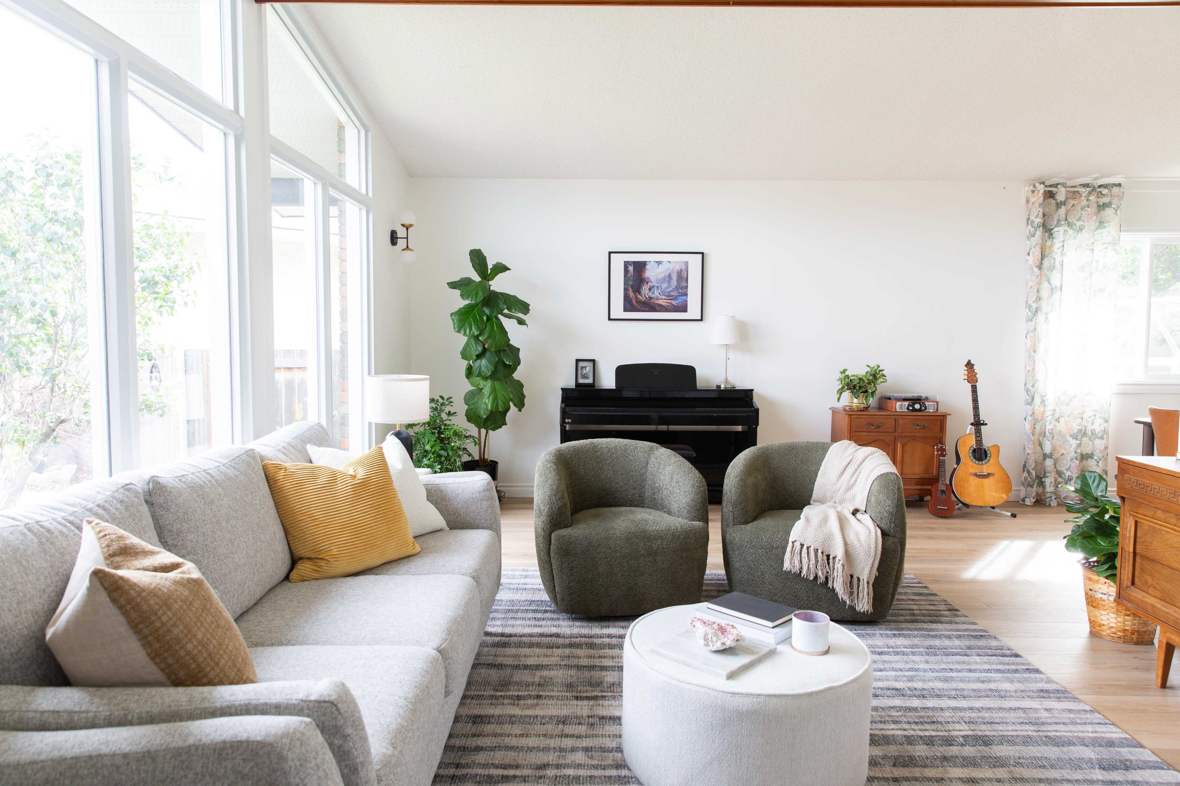 The scene features a modern living room with a gray sofa, two green armchairs, a piano, an acoustic guitar, and various plants.