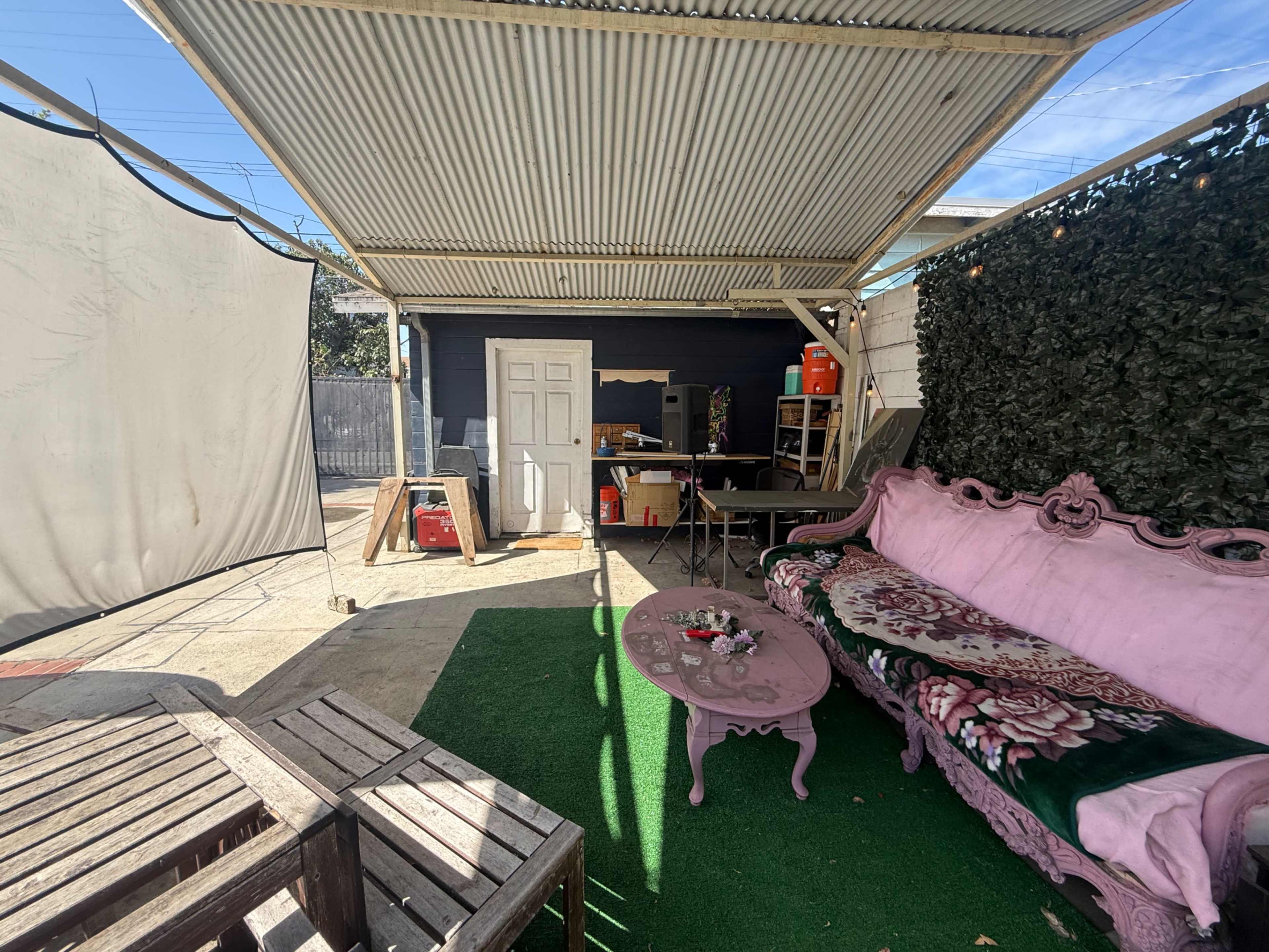 The image shows a shaded outdoor space with a pink couch, a small table, and a working area in the background.