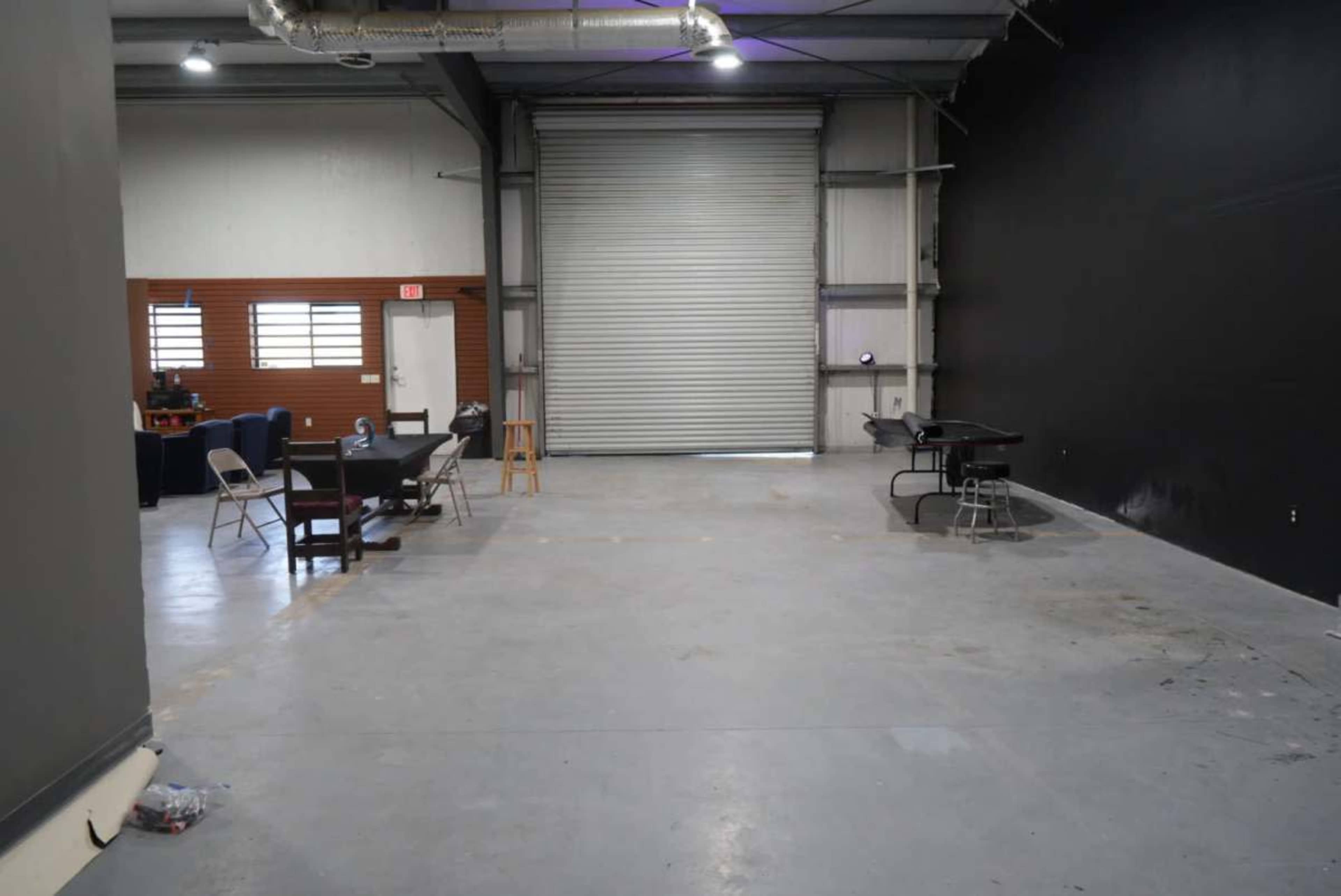 The image shows an empty industrial space with a concrete floor, a gray rolling door, and bare walls.