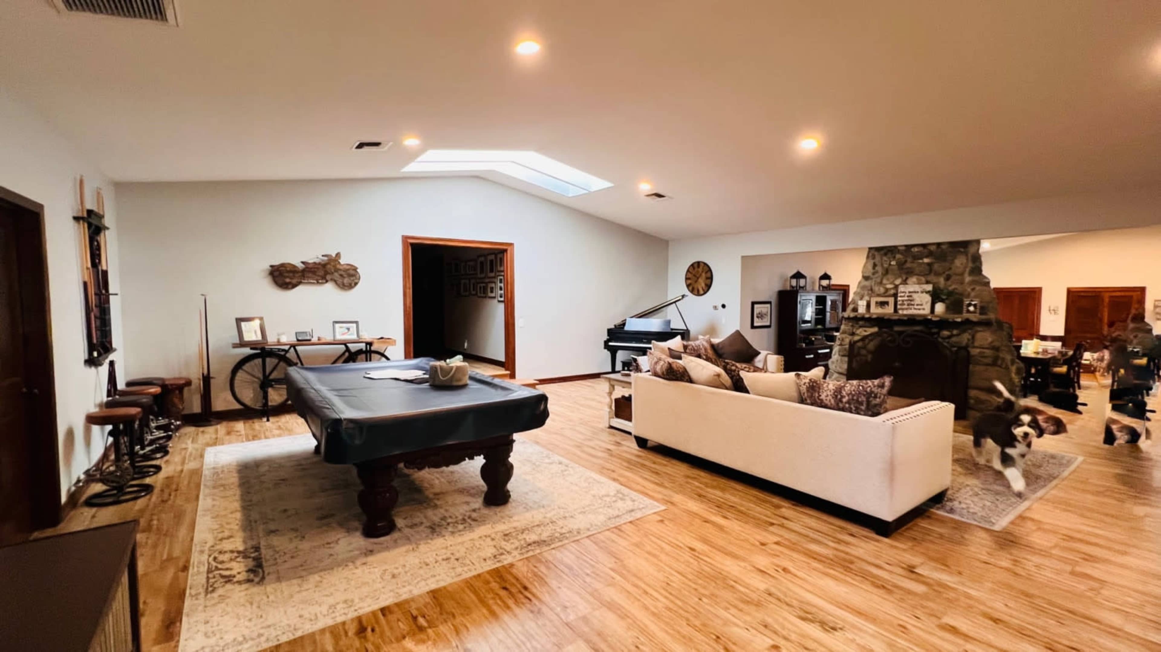 The spacious living area features a pool table, a couch, a stone fireplace, and a skylight.