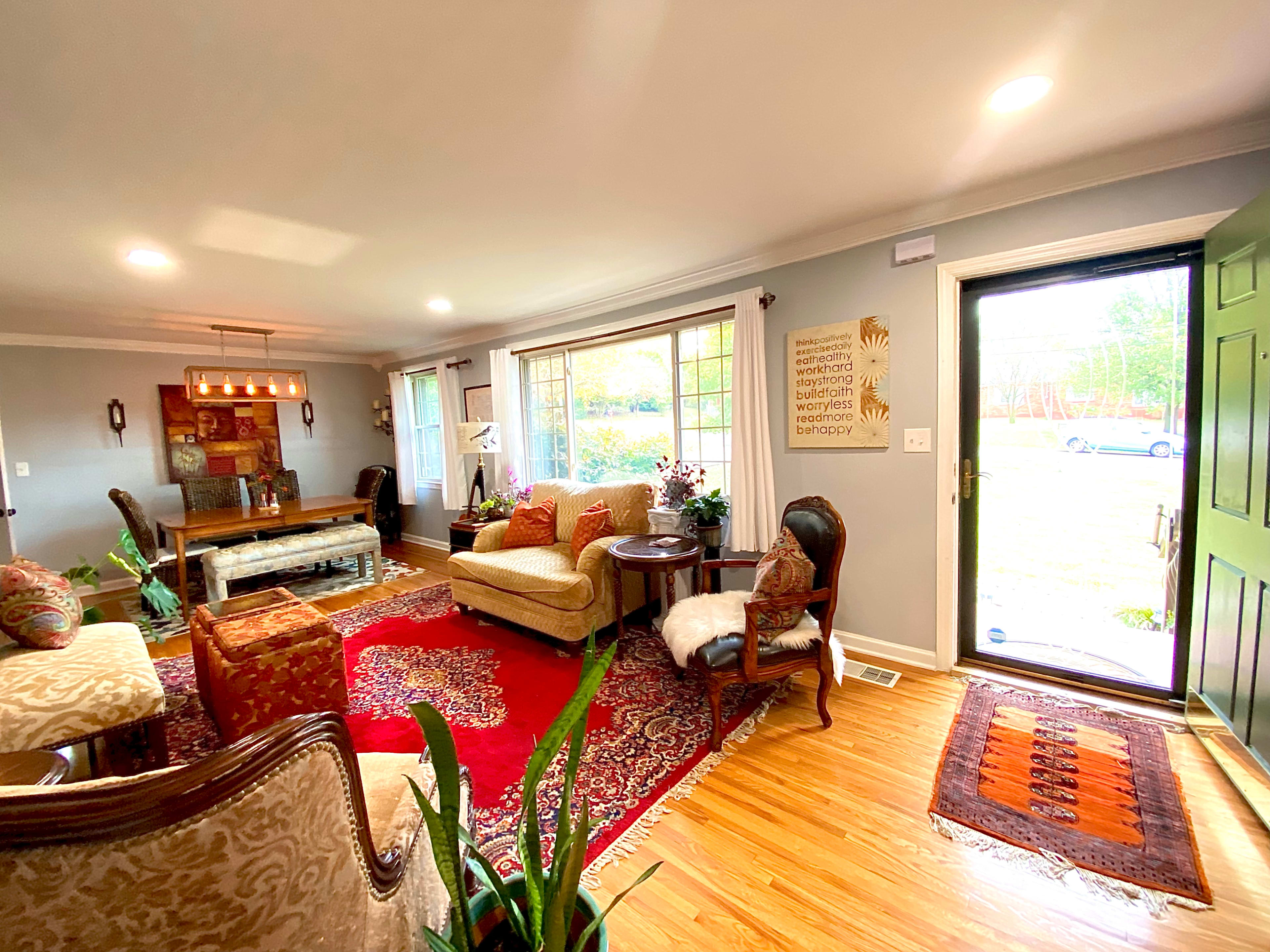 A well-lit living room features a mix of seating, a large area rug, and a view of the outdoors through a door and windows.