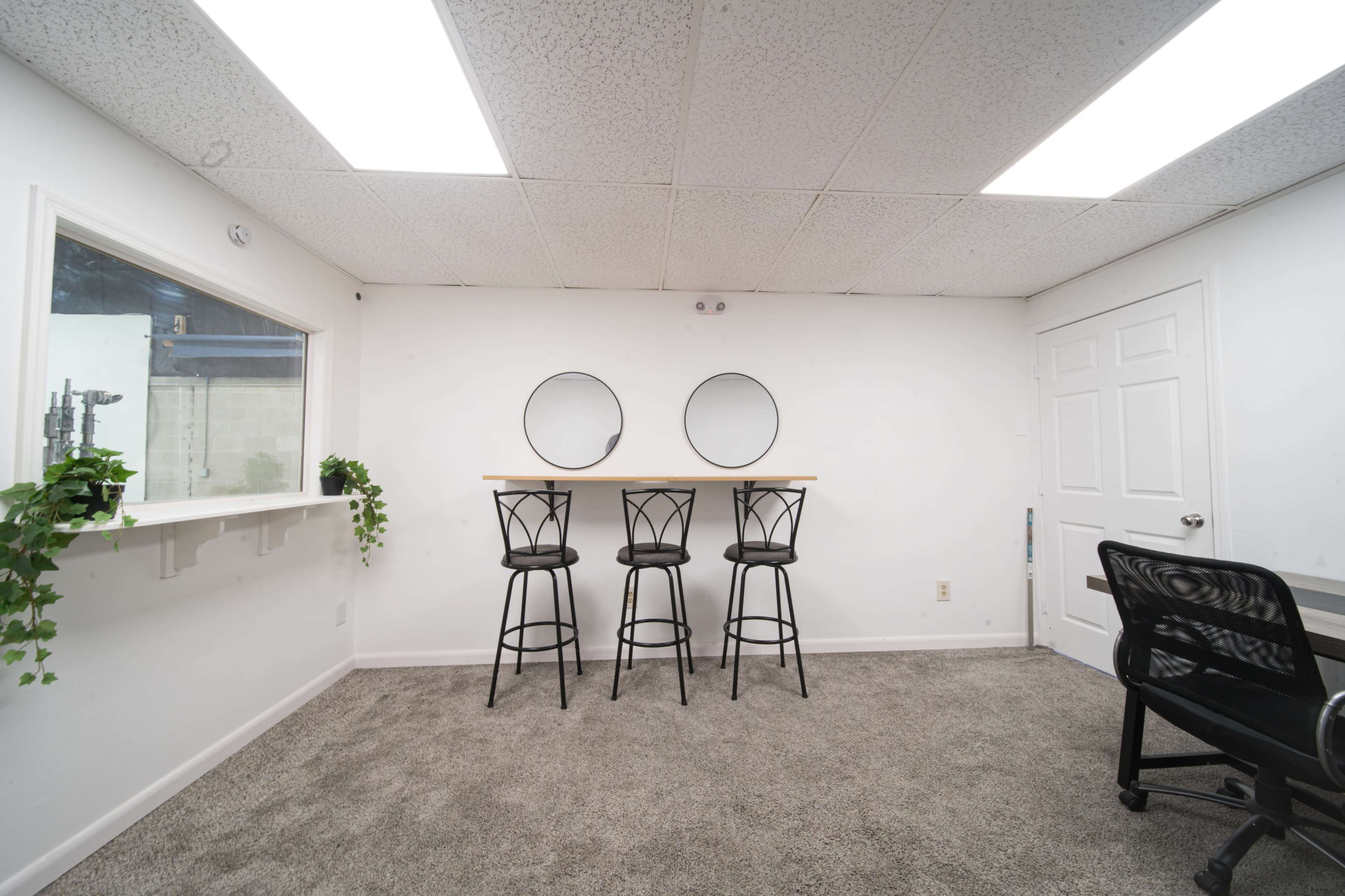 The image shows a small room with three high bar stools placed against a wall with two circular mirrors above a simple countertop.