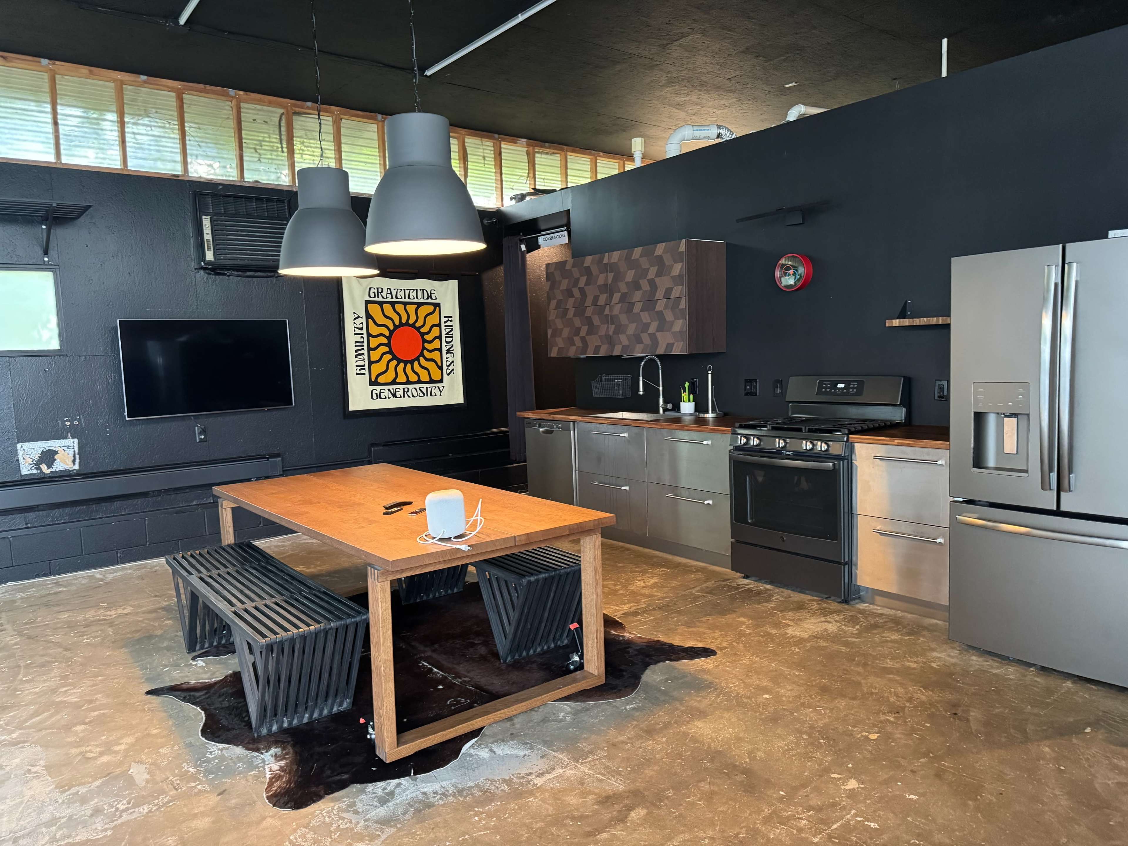 The image shows a modern kitchen with a black and wood color scheme, featuring a dining table, stainless steel appliances, and industrial-style light fixtures.