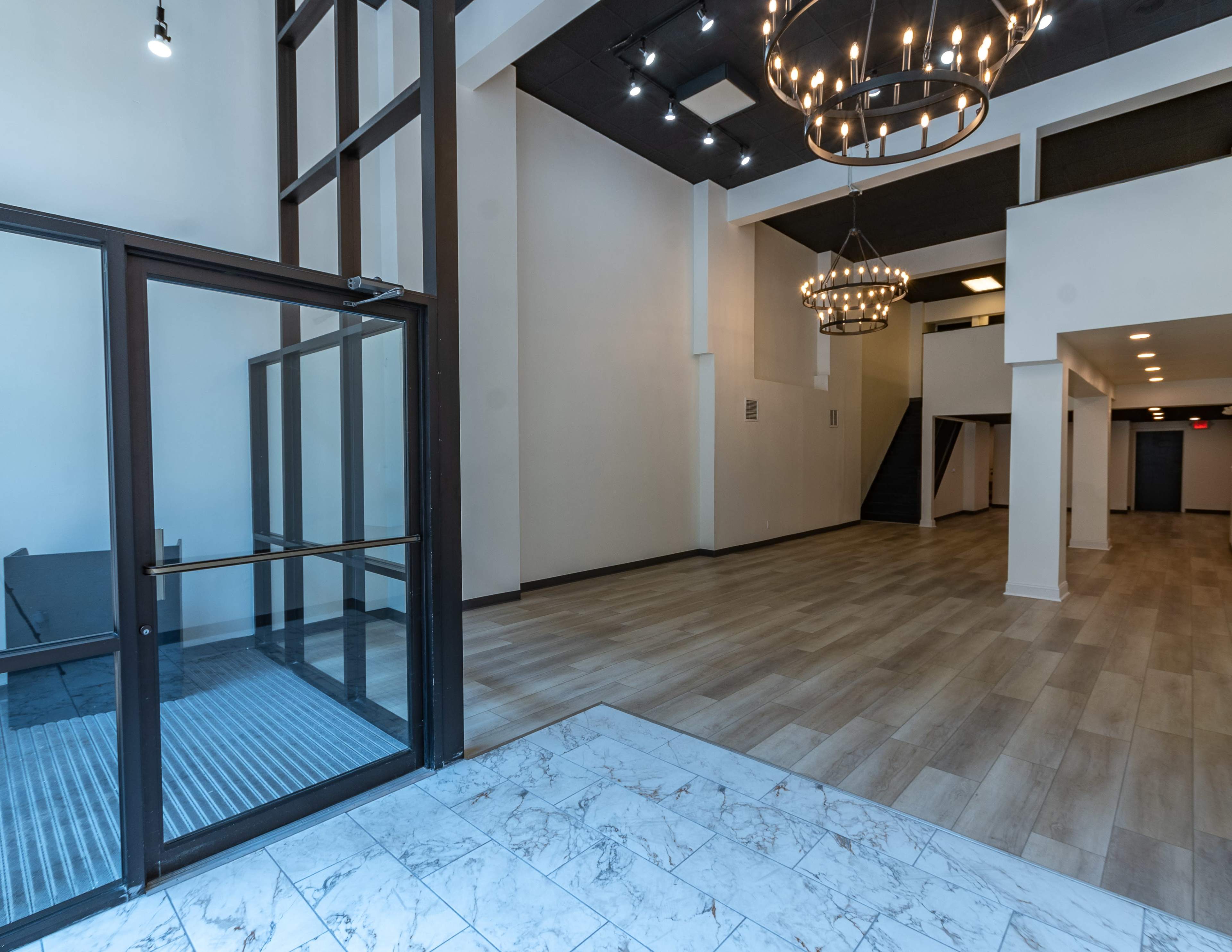 A spacious entryway with a staircase on one side, modern lighting fixtures, and a combination of tile and wood flooring.