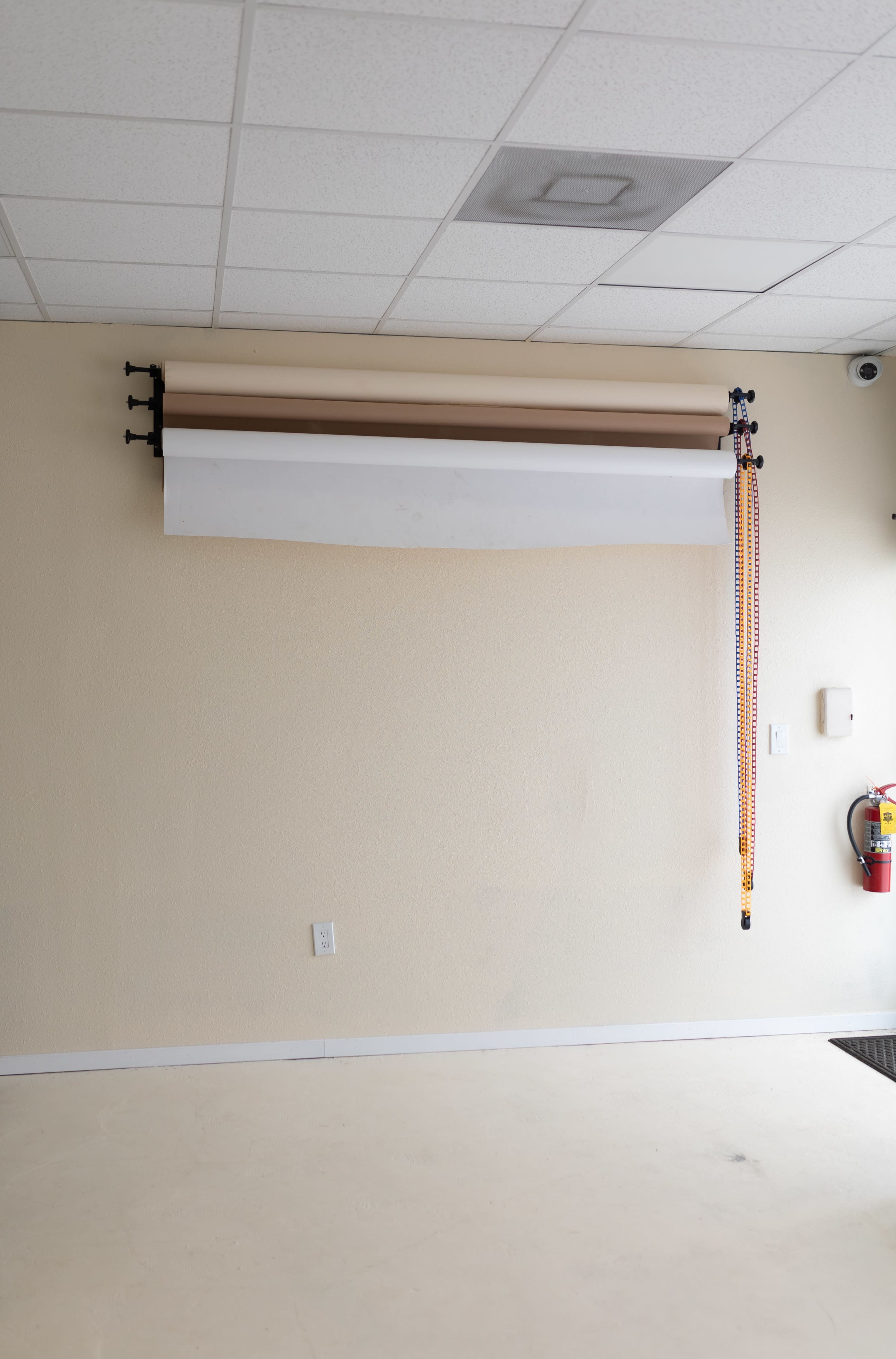 A blank wall features a mounted roll of paper backdrop and a fire extinguisher.