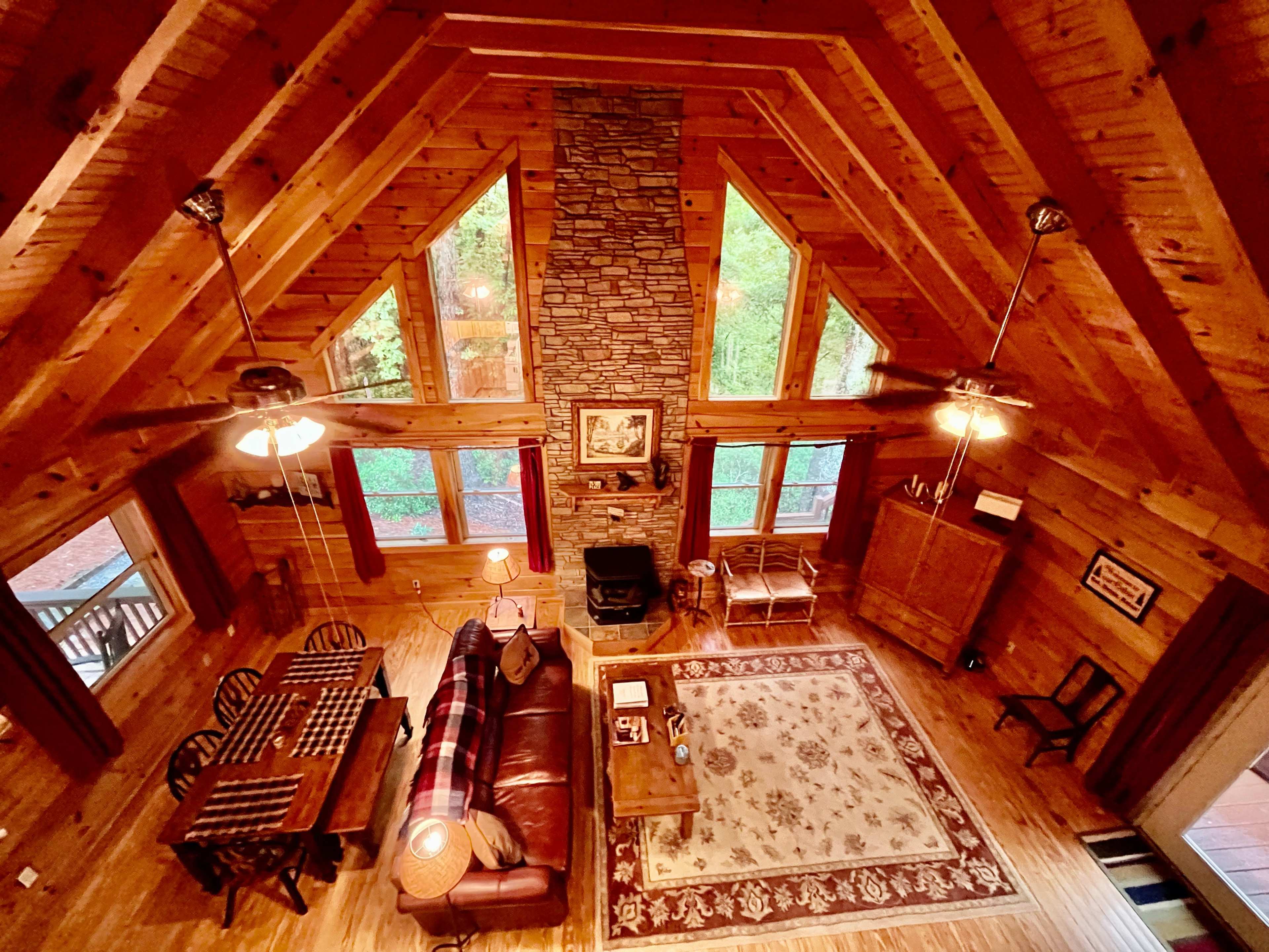 A spacious wooden cabin interior with large windows, a stone fireplace, and a dining table set for game playing.