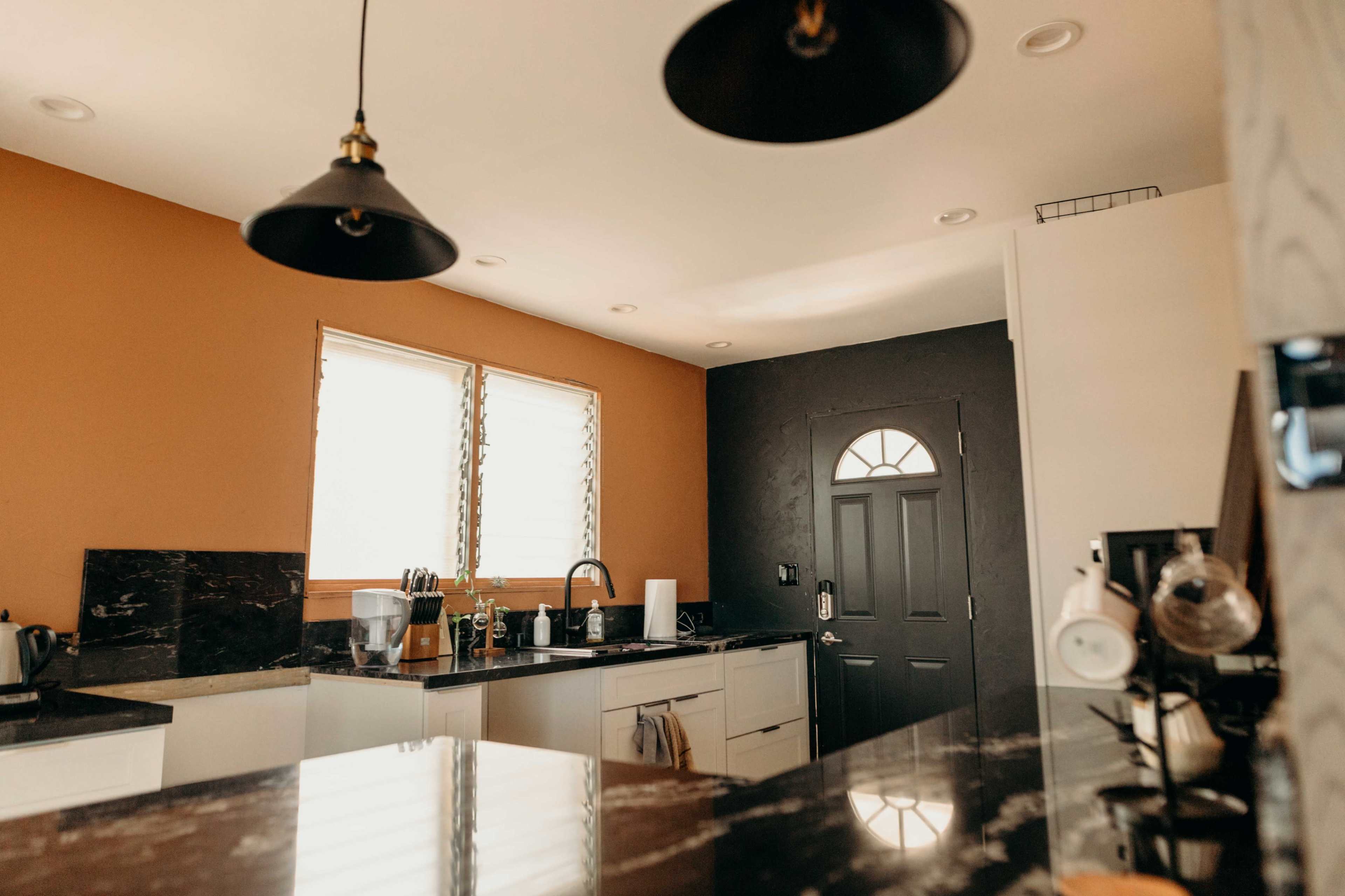 A kitchen with a dark door, large windows, and a mix of light and dark cabinetry.