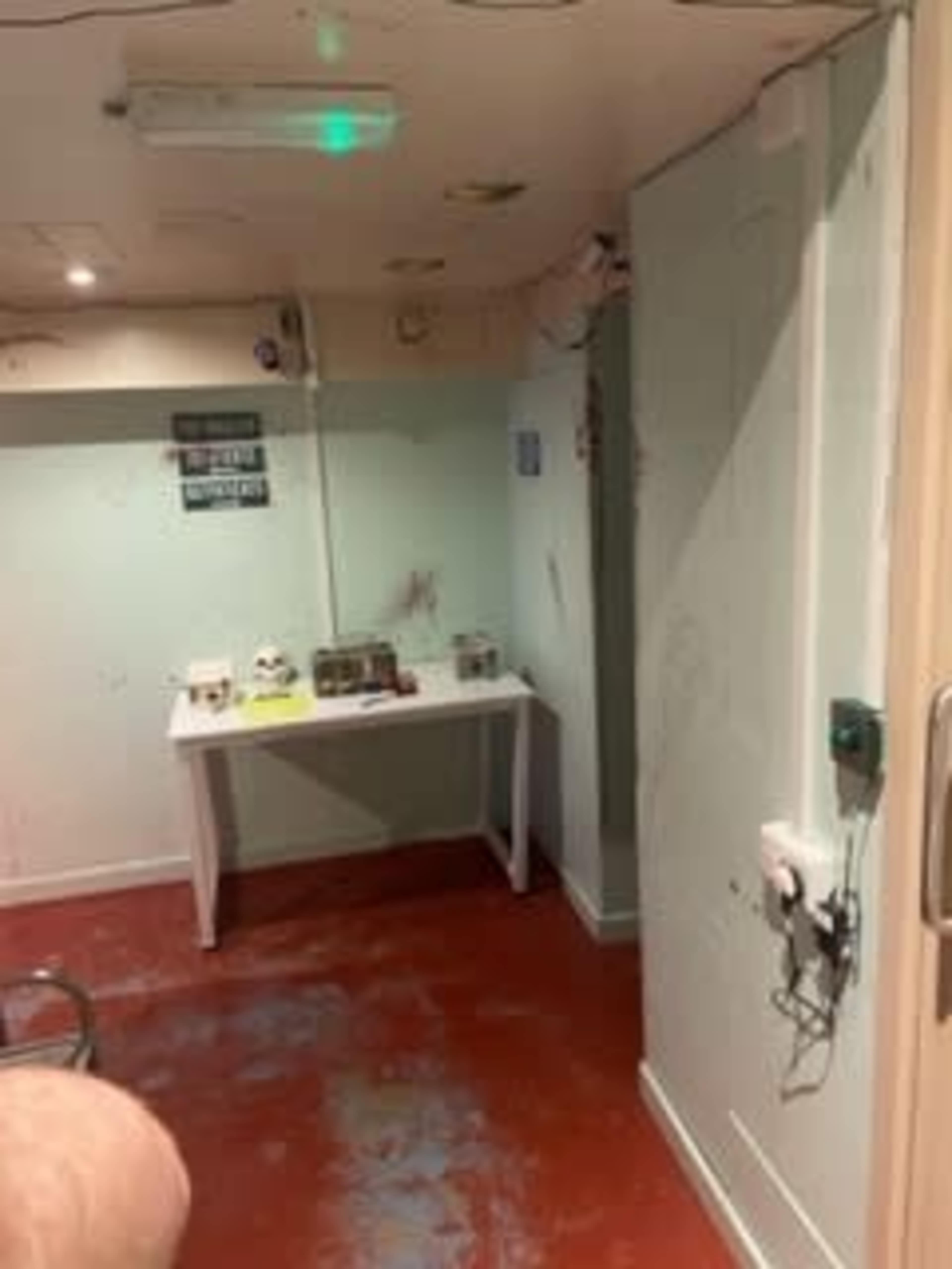 A small, dimly lit room with a red floor, a white table against the wall, and exposed wires on the ceiling.
