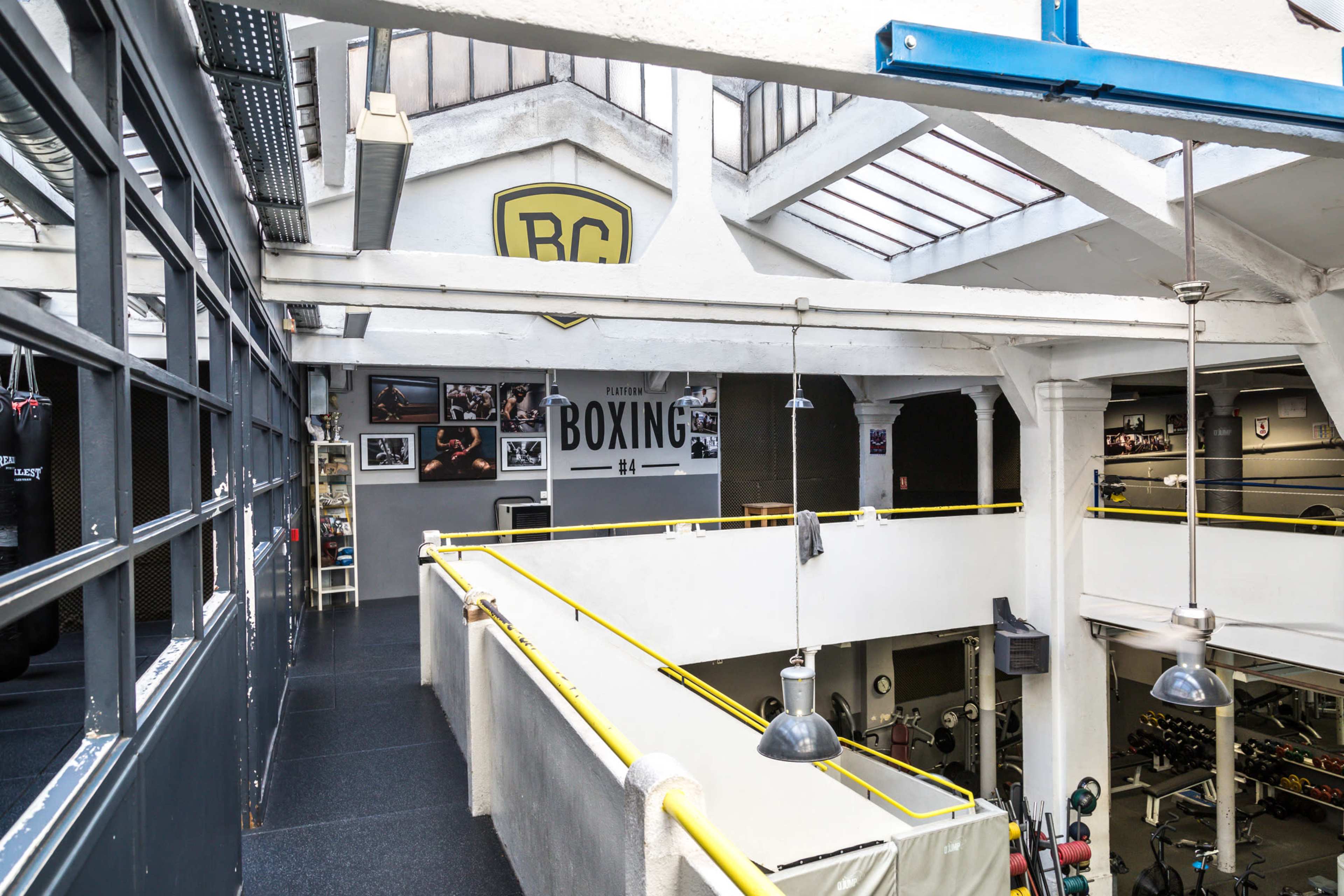 A spacious gym with boxing equipment and workout areas, featuring high ceilings and large windows.