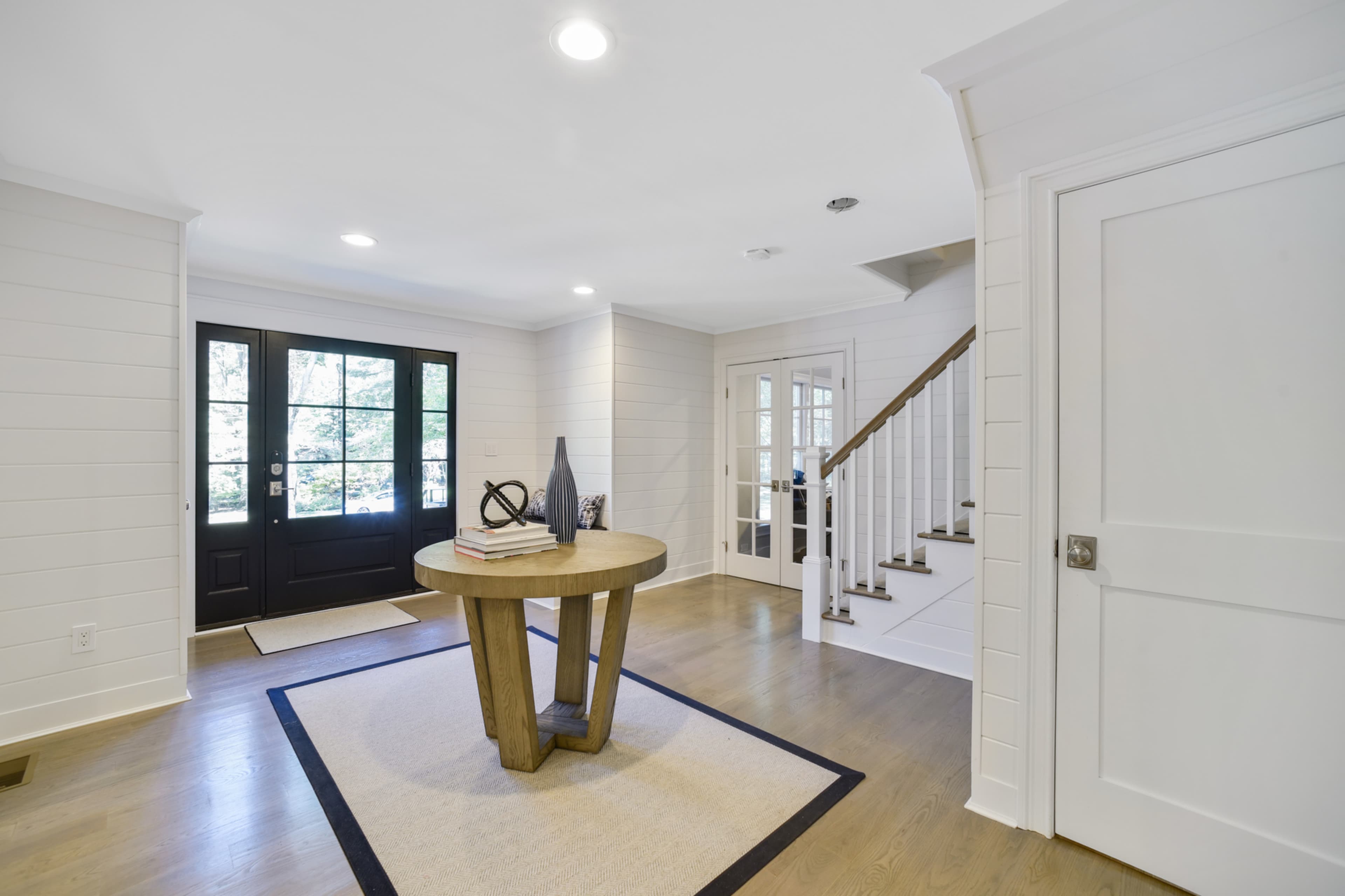 A bright entryway with a round wooden table, a rug, and a staircase leading to an upper level.