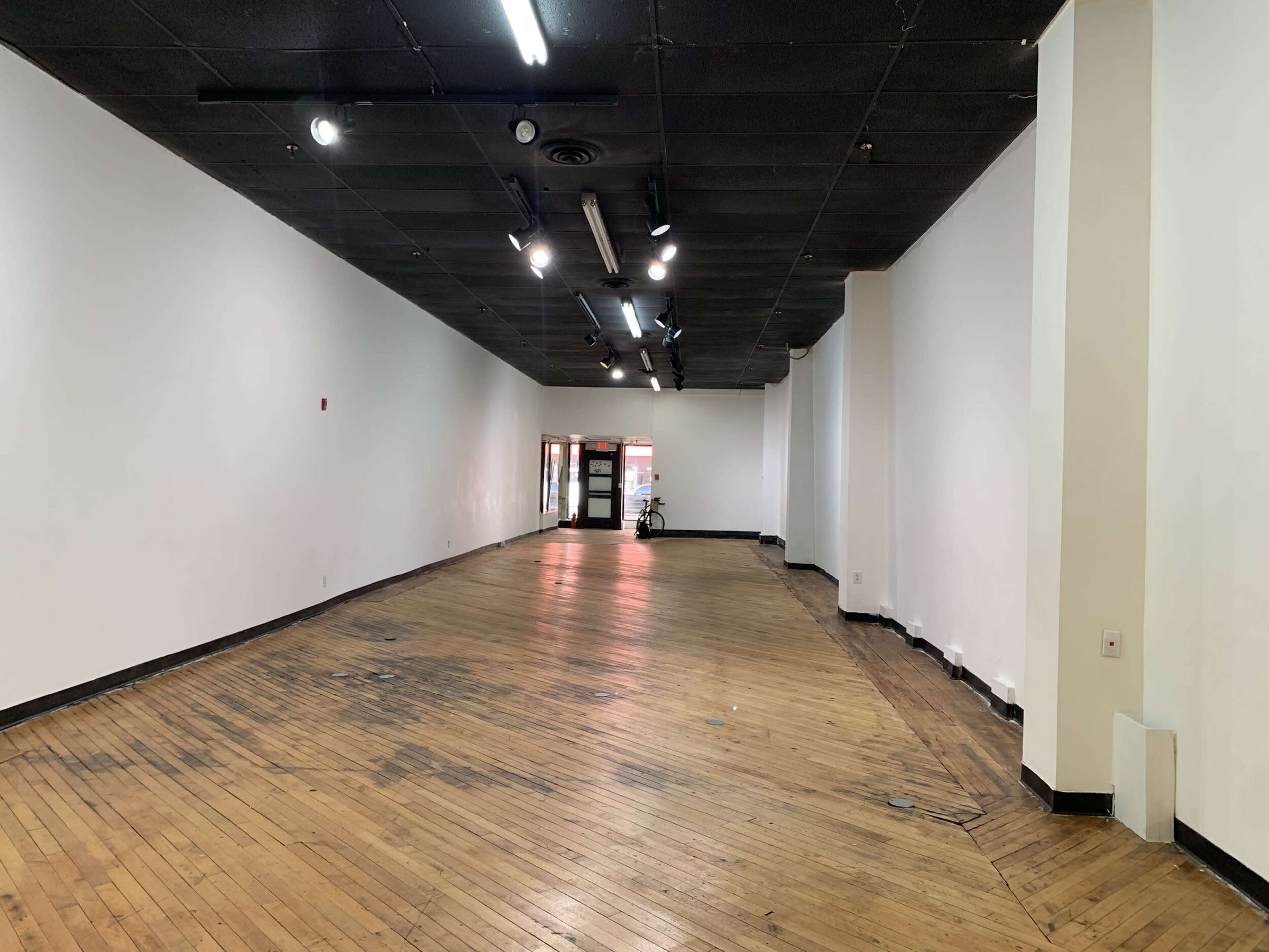 A spacious, empty room with wooden floors and fluorescent lighting.