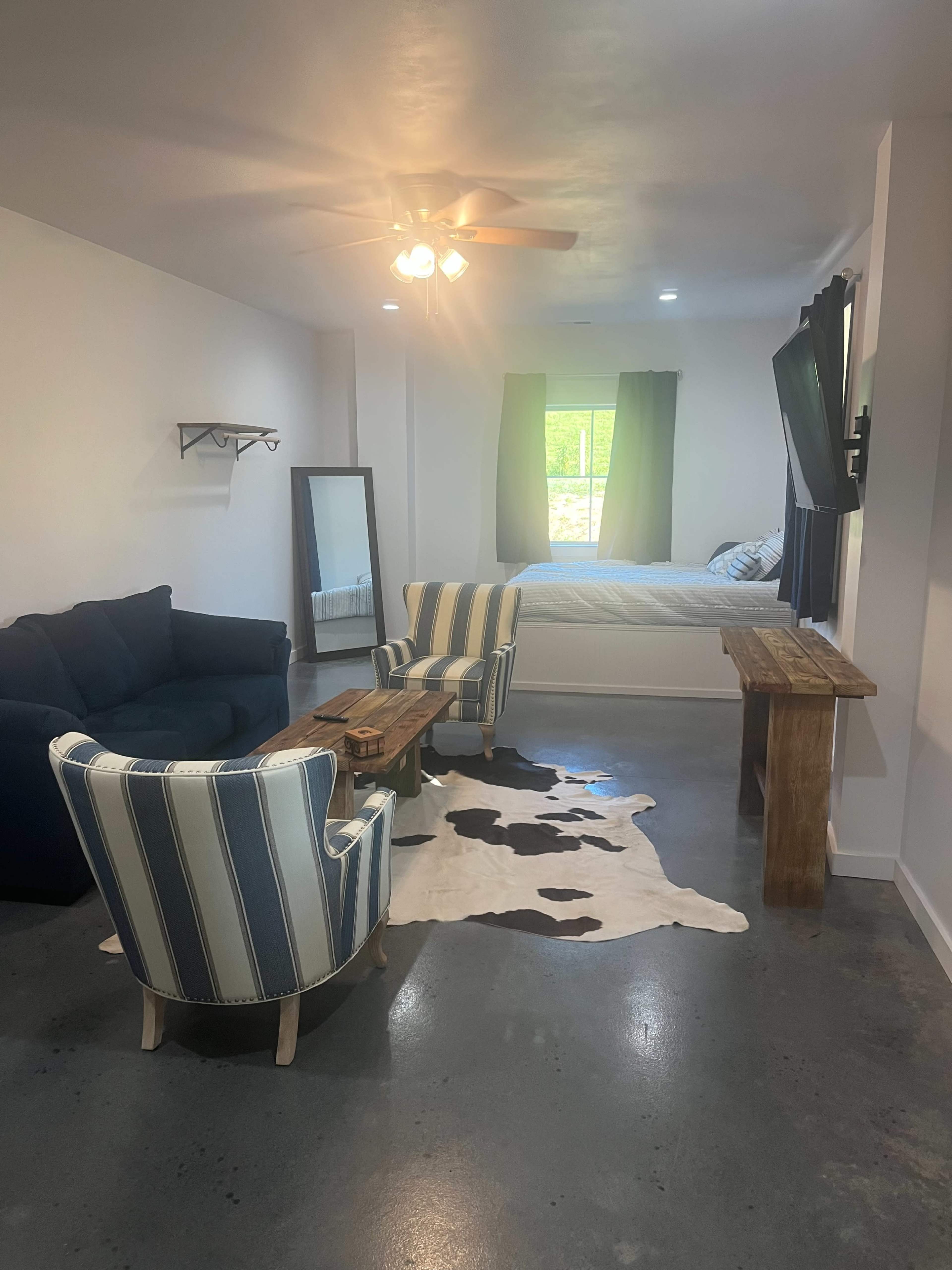 A living space featuring a blue sofa, striped chairs, a wooden coffee table, and a bed in the background.