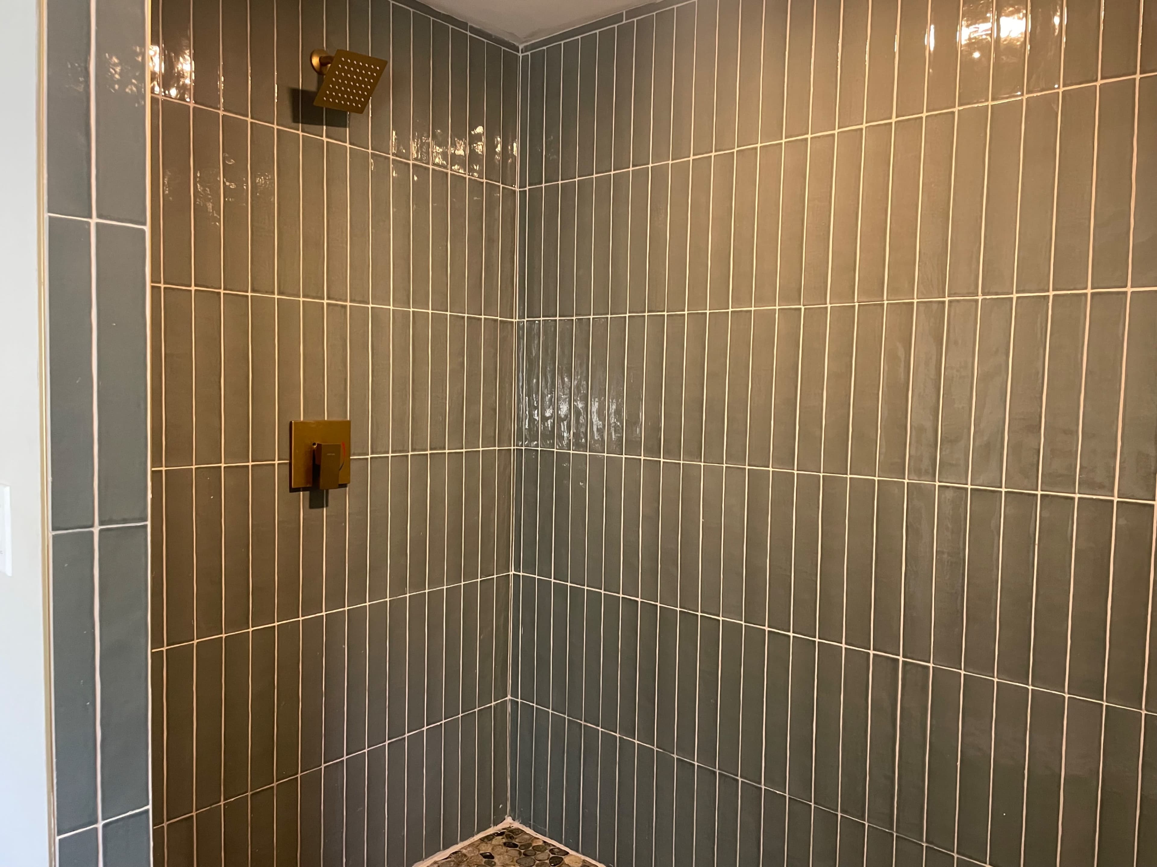 The image shows a modern shower with vertical gray tiles and a rainfall showerhead.
