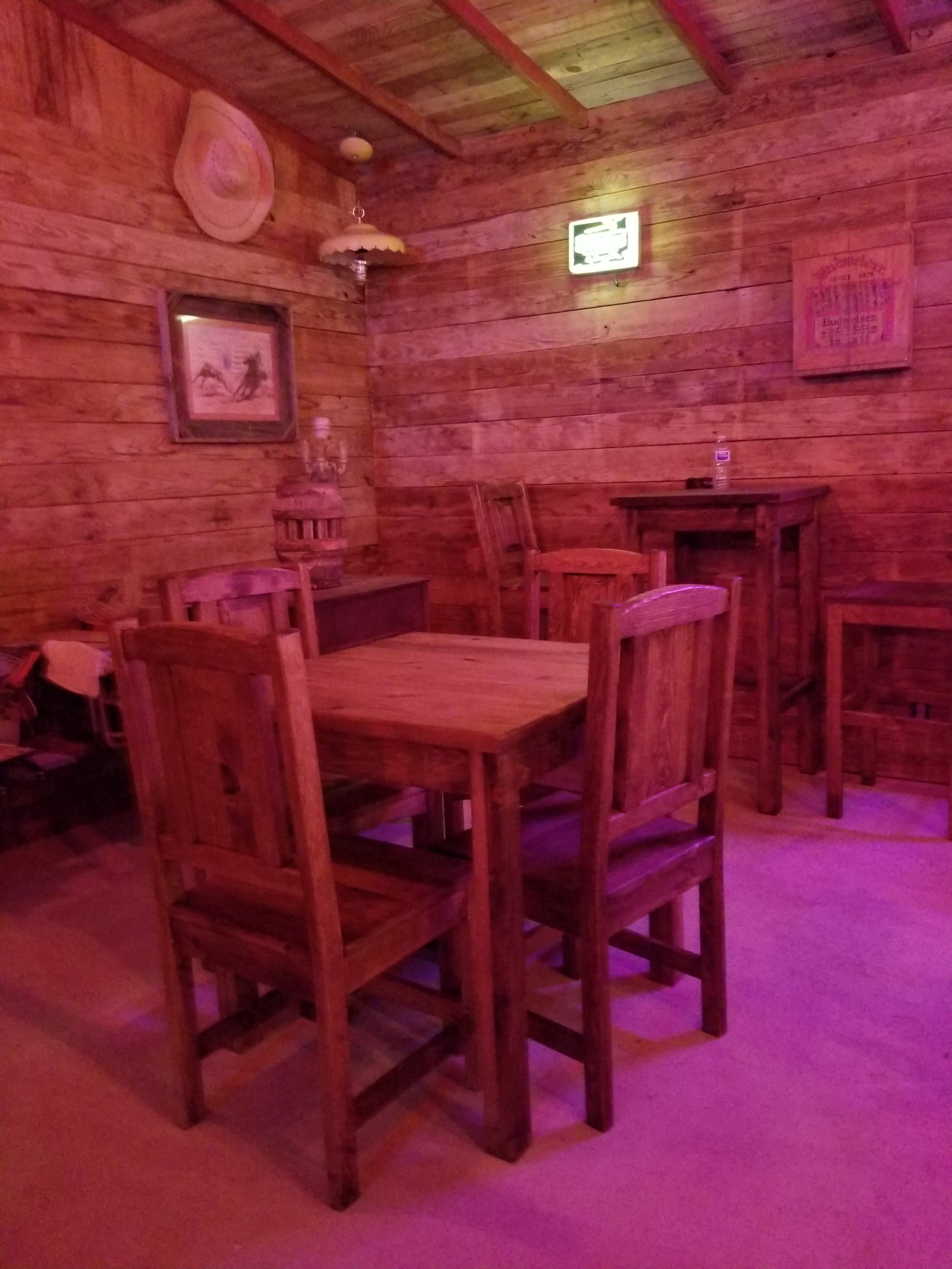 A rustic wooden interior with a small table surrounded by chairs, illuminated by soft lighting.