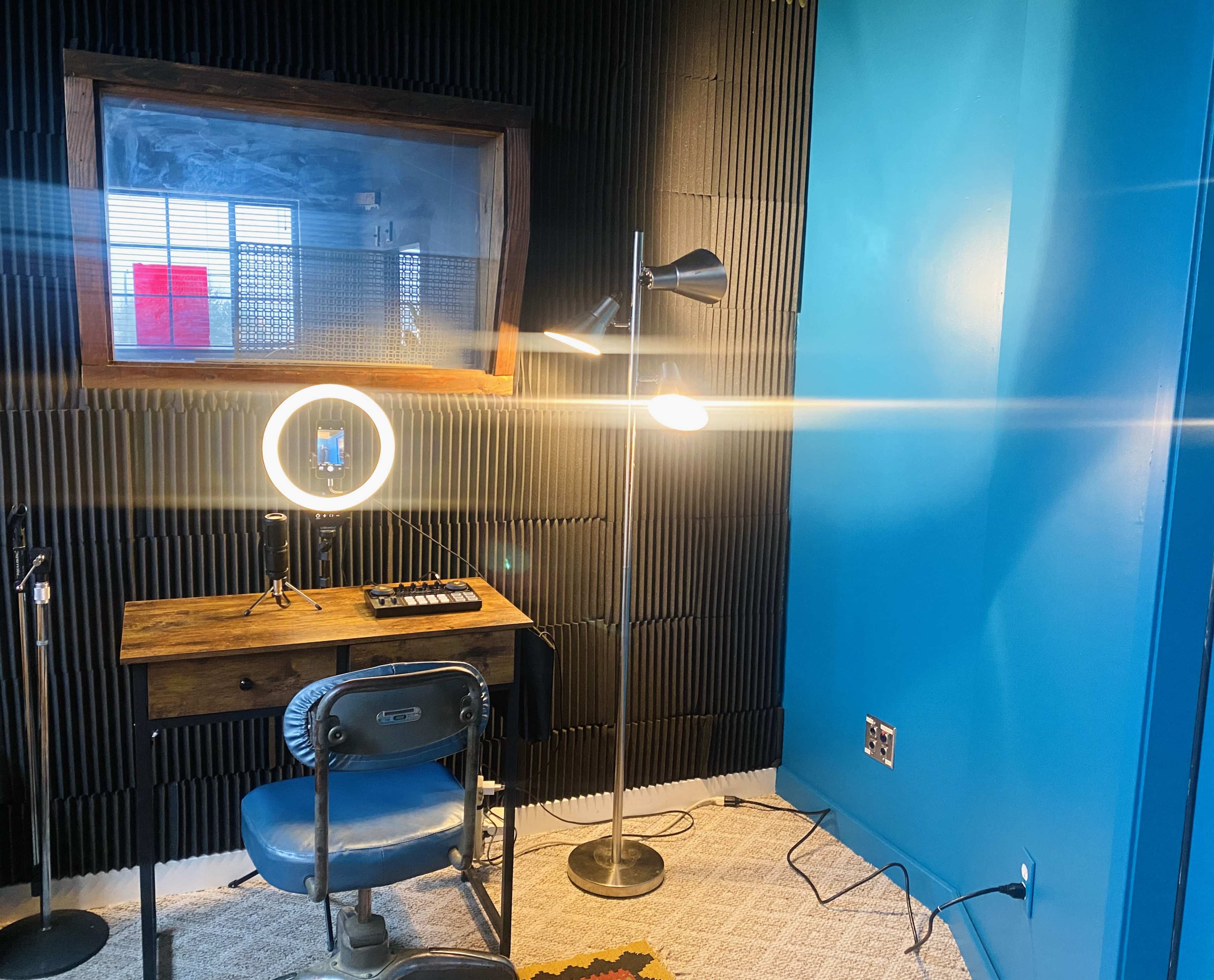 The image shows a small room with a desk, a circular LED lamp, and a floor lamp, featuring soundproofed walls and a blue accent wall.