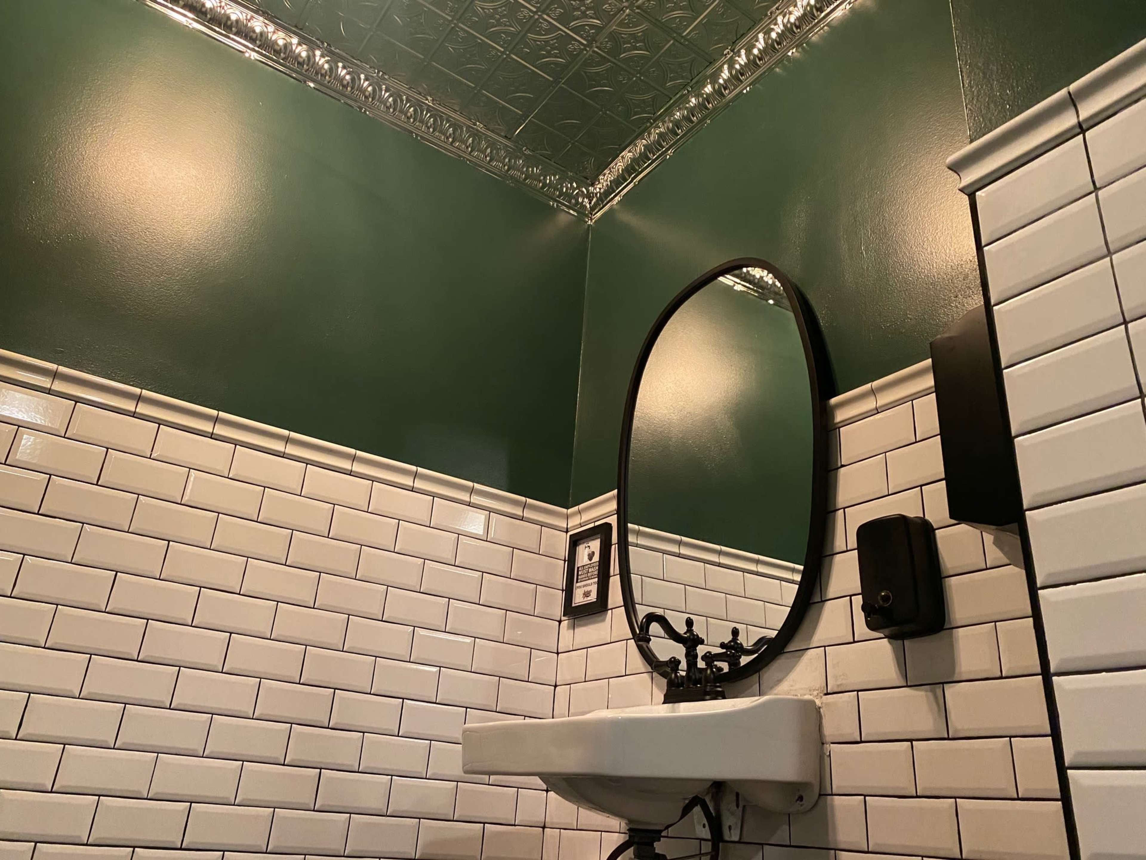 A small bathroom with a green-painted wall, a white tiled sink, and a round black-framed mirror.