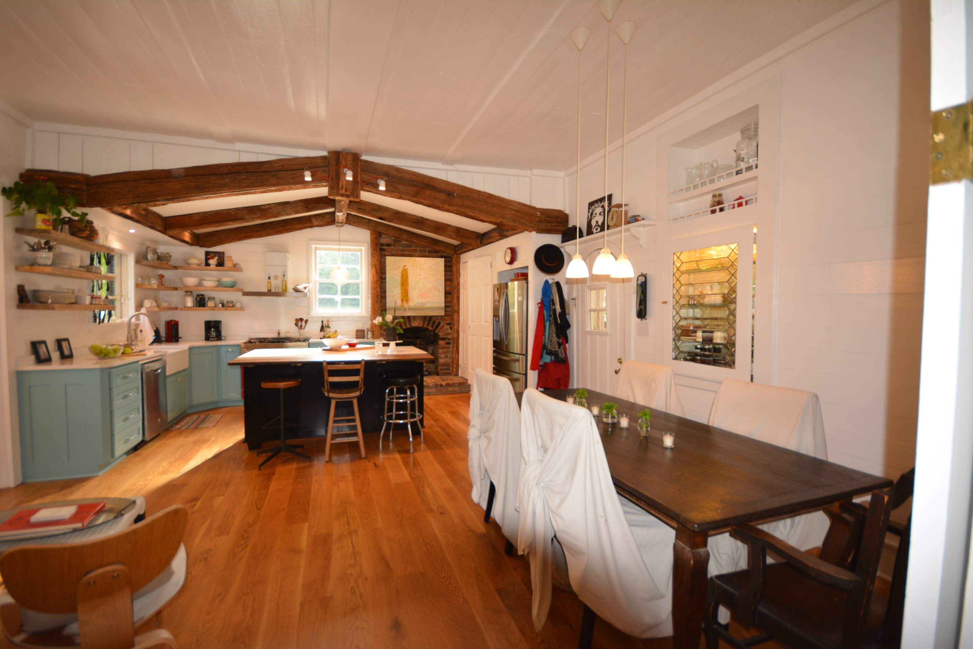The image shows a spacious kitchen and dining area featuring wooden beams, a central island, and a dining table set with chairs.