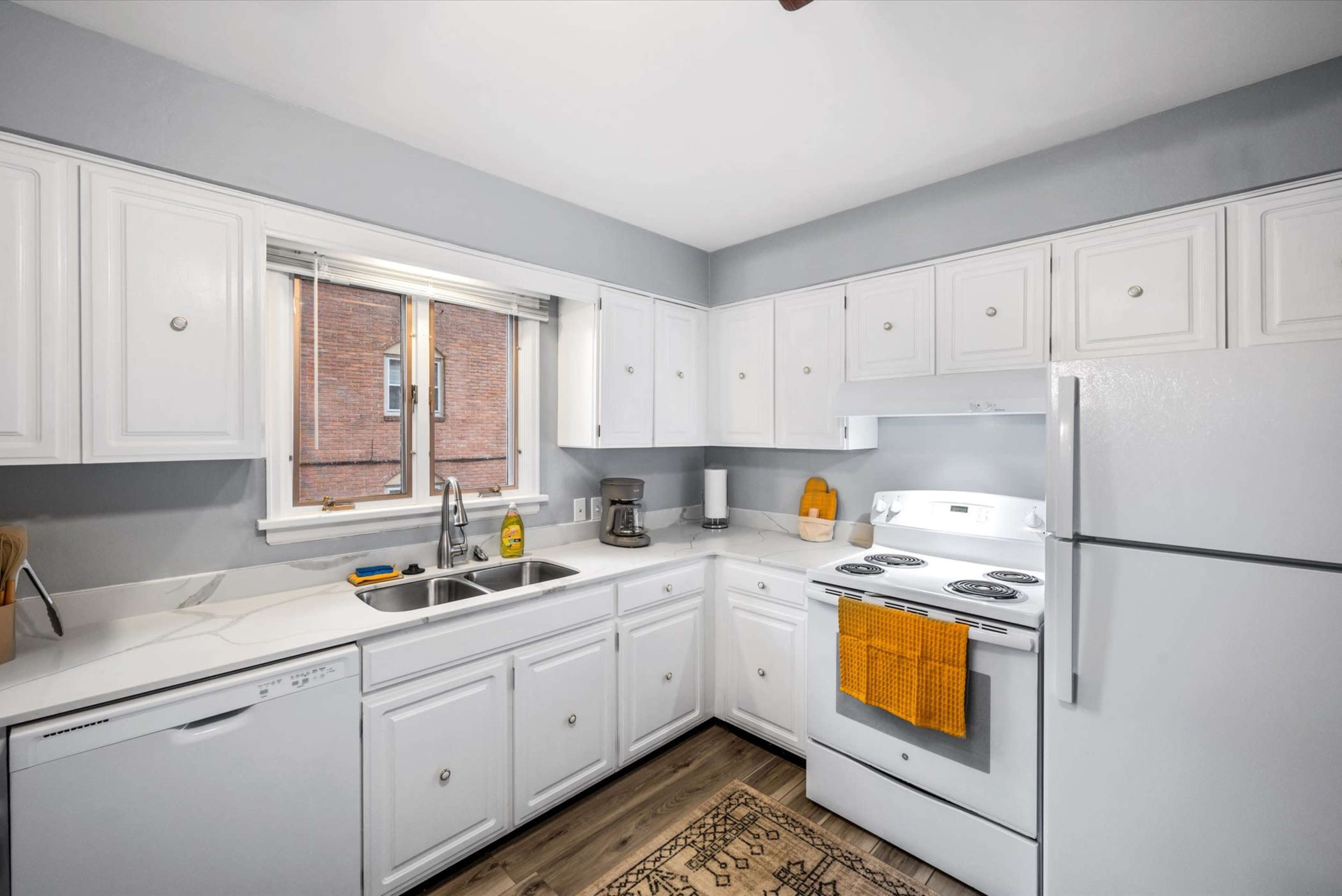 A clean kitchen with white cabinets, a white countertop, a window over the sink, and an oven with a stovetop.