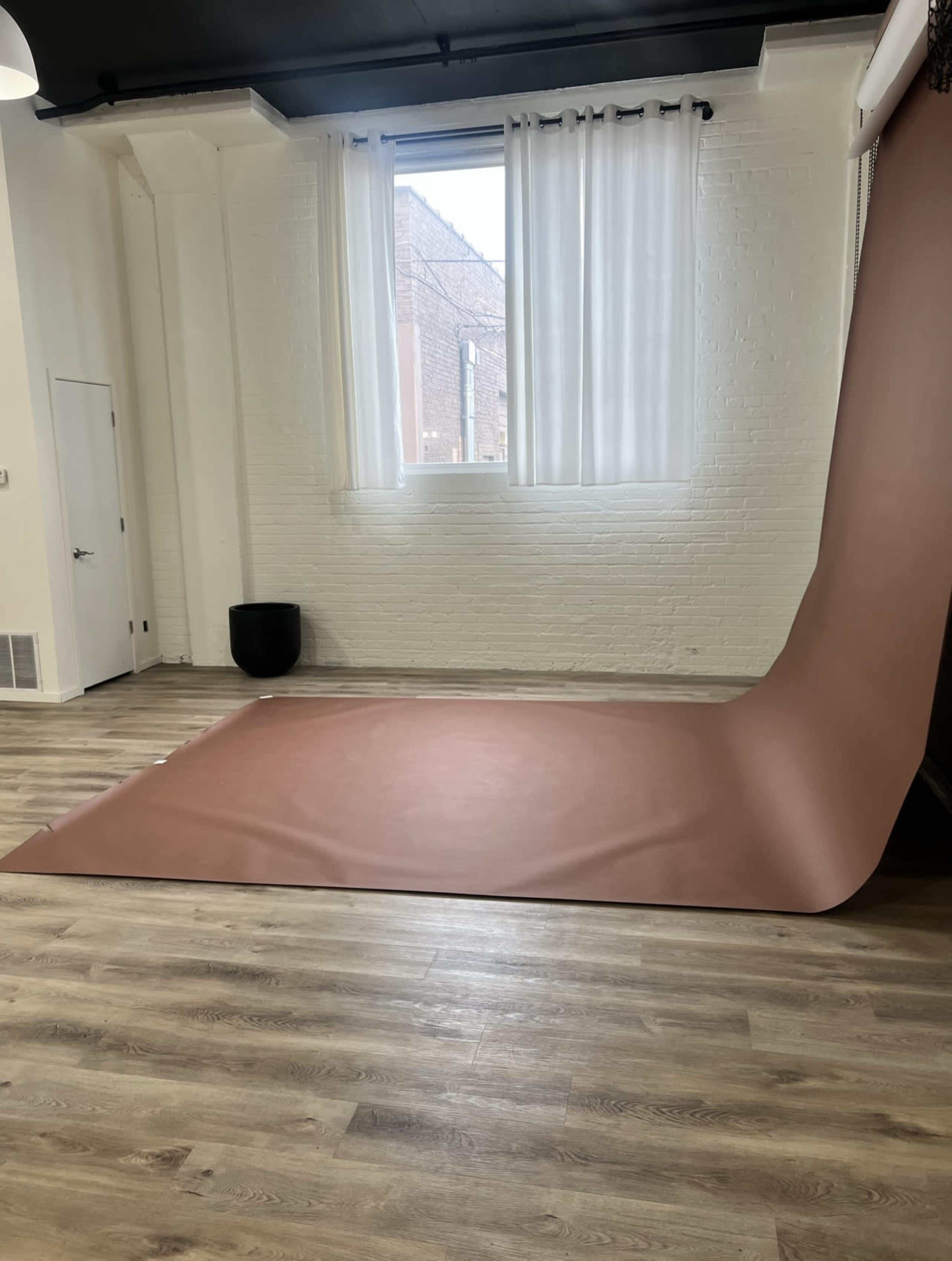 The image shows a spacious studio with a large, rolled-out brown backdrop on the wooden floor, illuminated by natural light from a window.