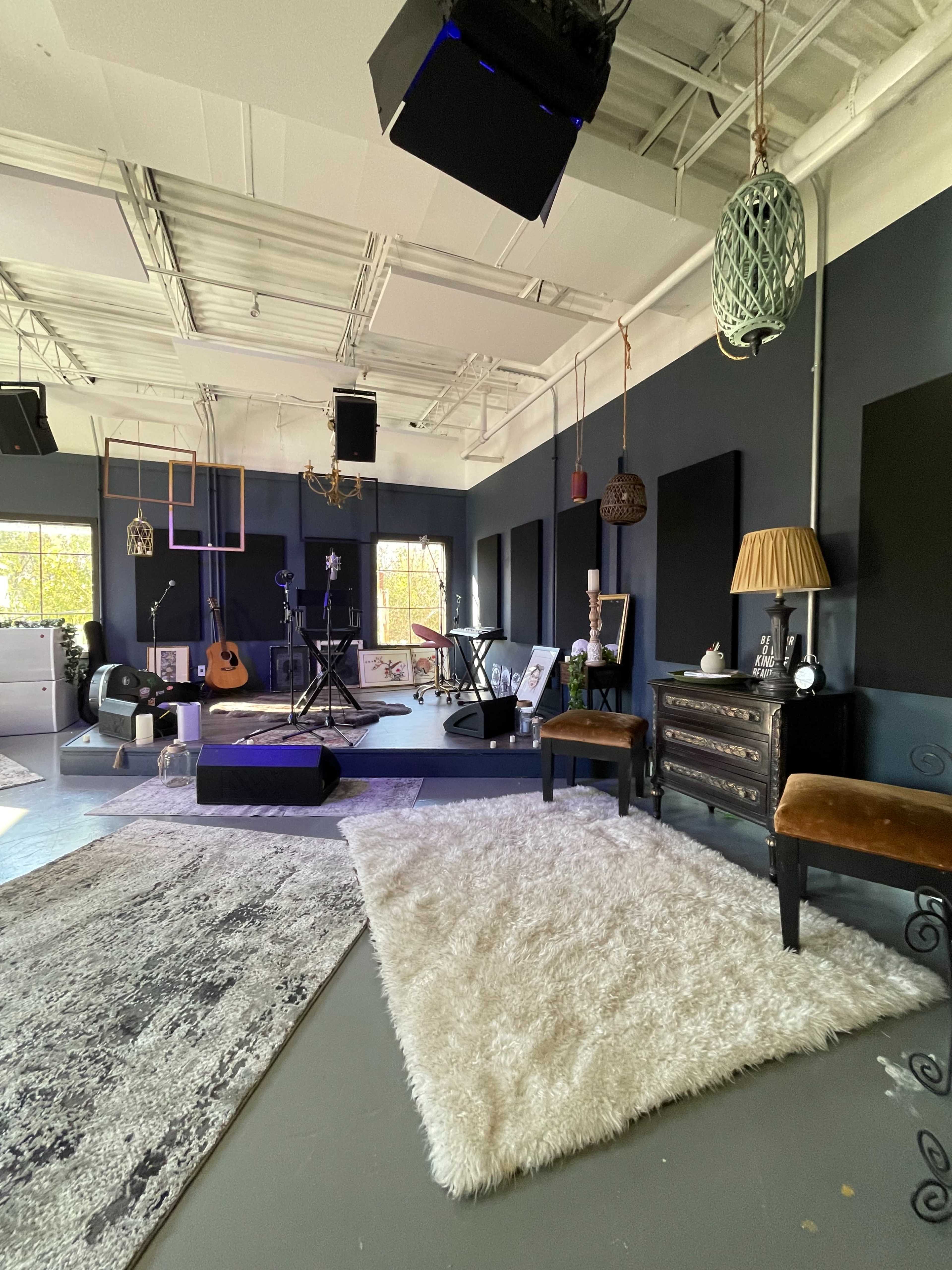 The image shows a spacious music studio with musical instruments, a patterned rug, and various pieces of furniture arranged throughout the room.