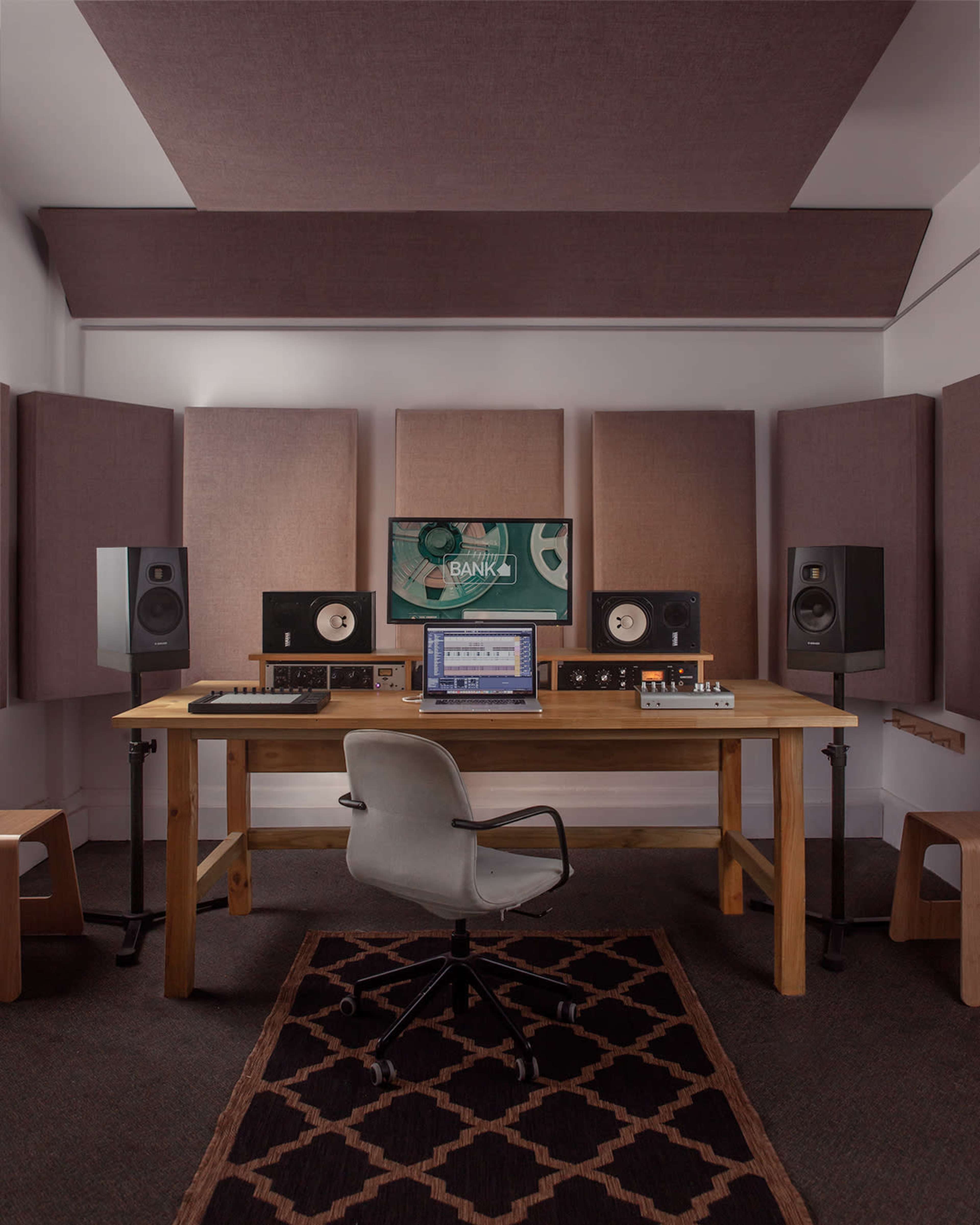 A minimalist music production studio features a wooden desk with a computer and audio equipment, flanked by soundproof panels and speakers.