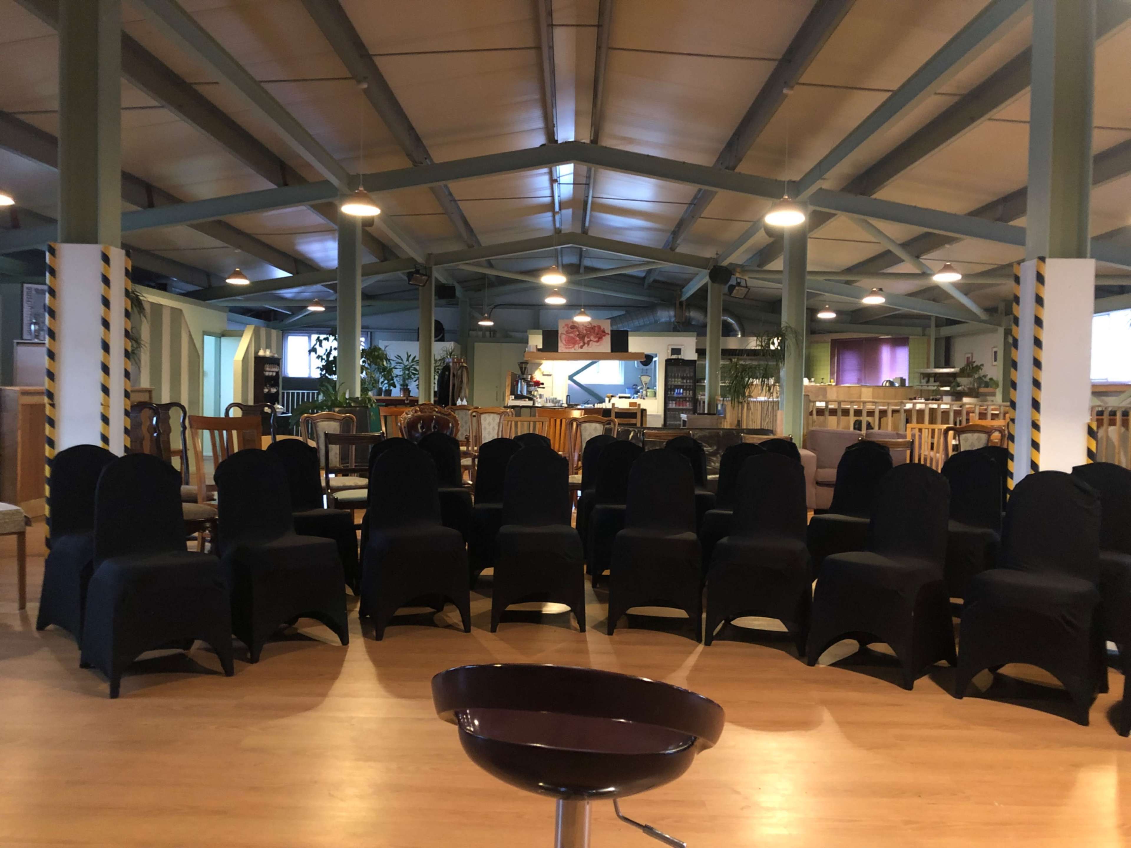 A rows of chairs covered in black fabric arranged in a seating area of a spacious room with high ceilings and wooden flooring.