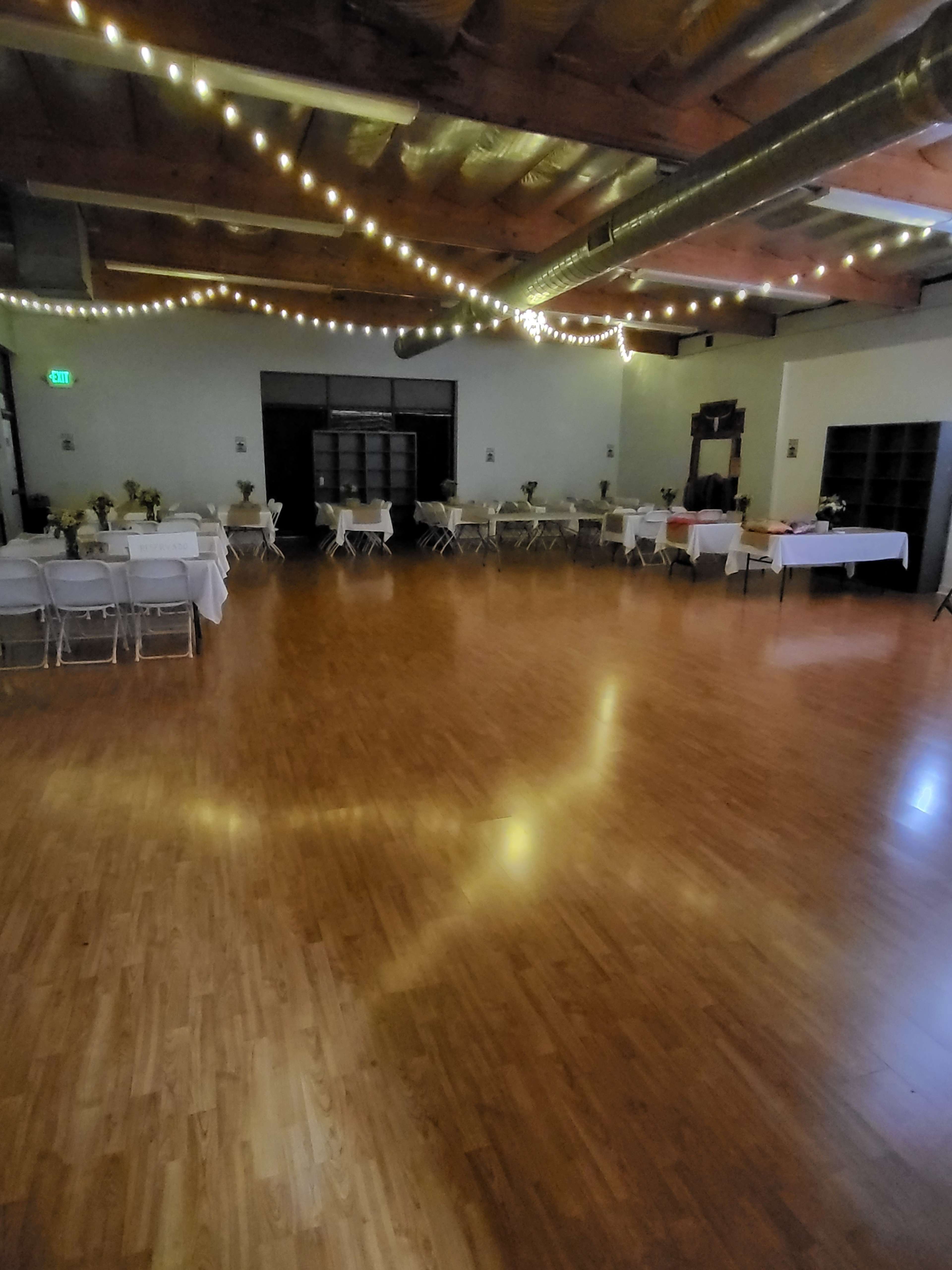 An empty event space with tables set up and string lights hanging from the ceiling.
