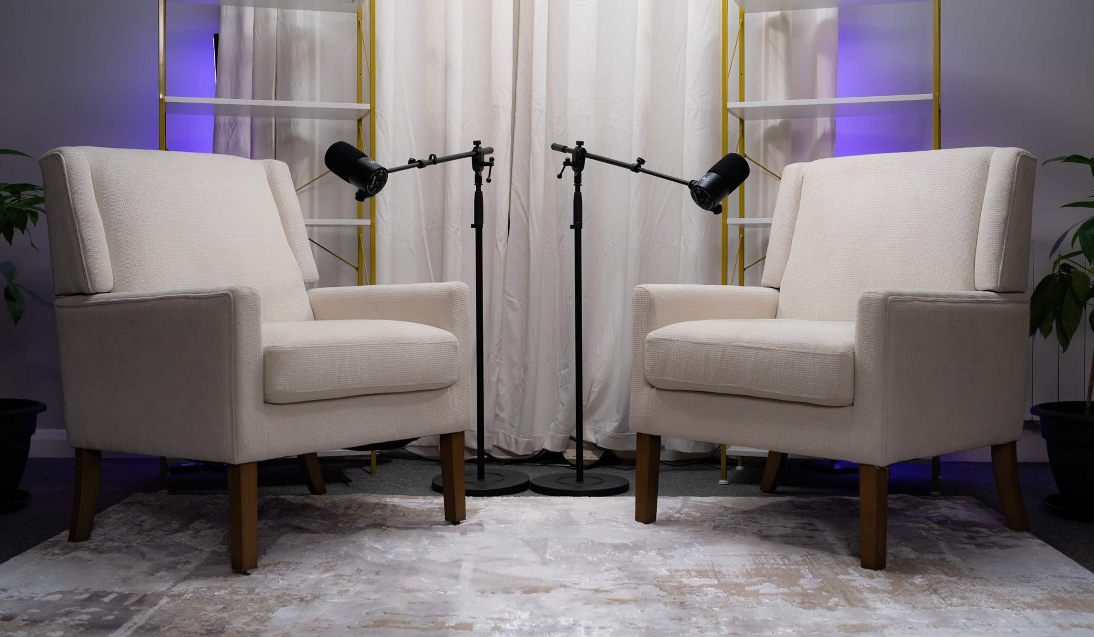 The image shows two cream-colored chairs positioned across from each other on a patterned rug, with floor lamps standing between them and a backdrop of curtains.