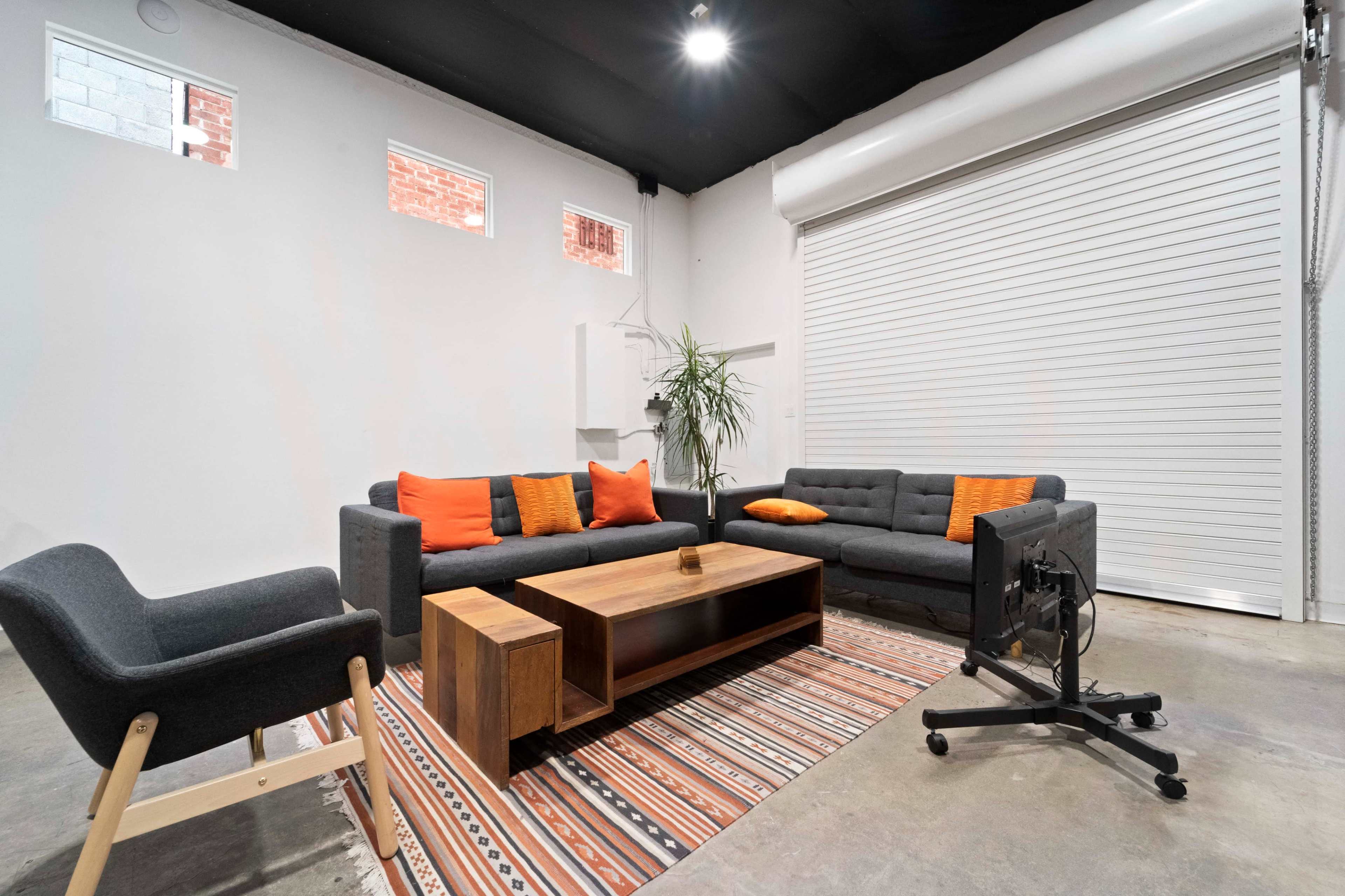A modern lounge area features two sofas, a coffee table, and a chair set against a white wall with a roll-up door.