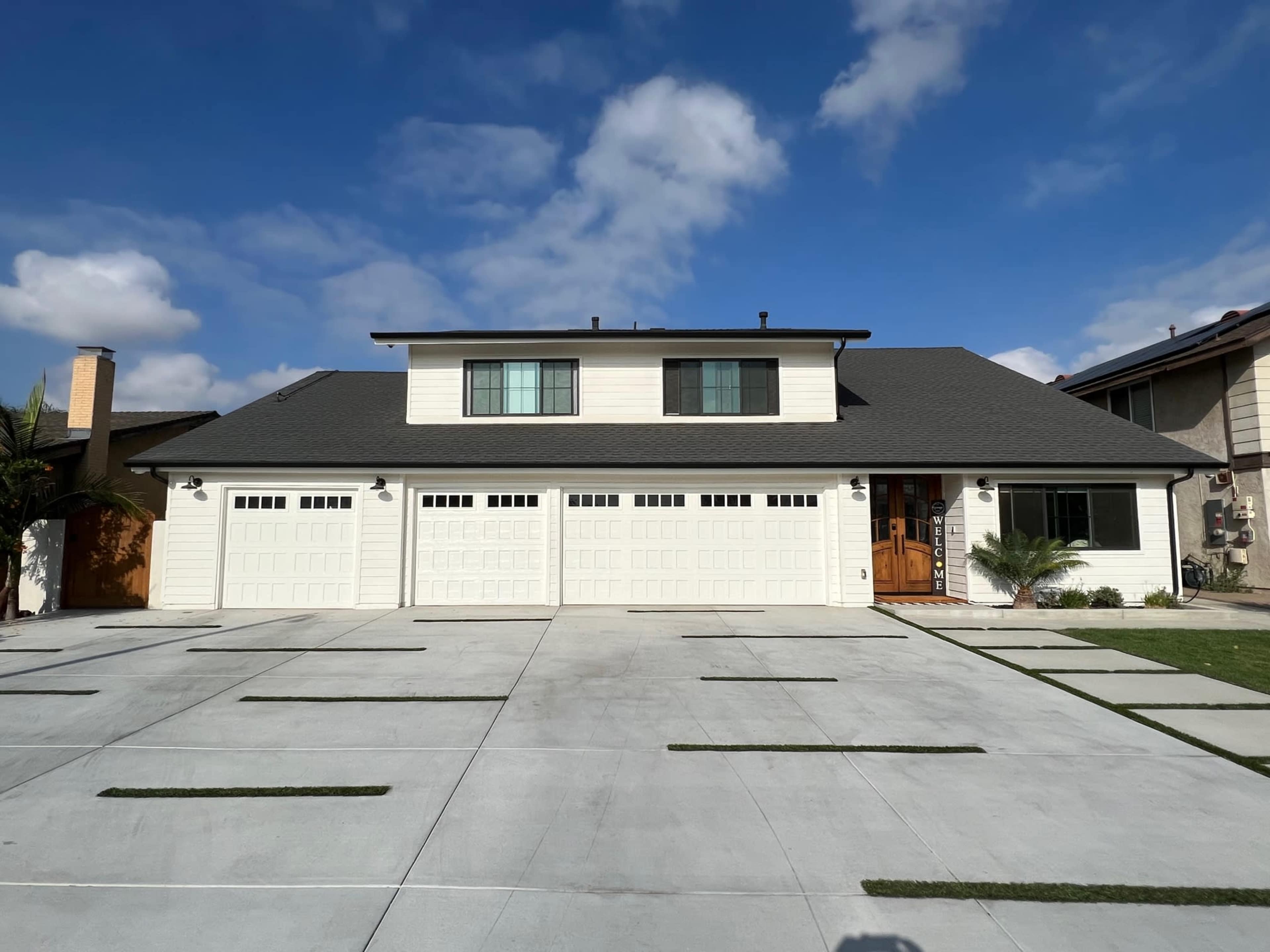A two-story residential house with a large paved driveway and multiple garage doors.