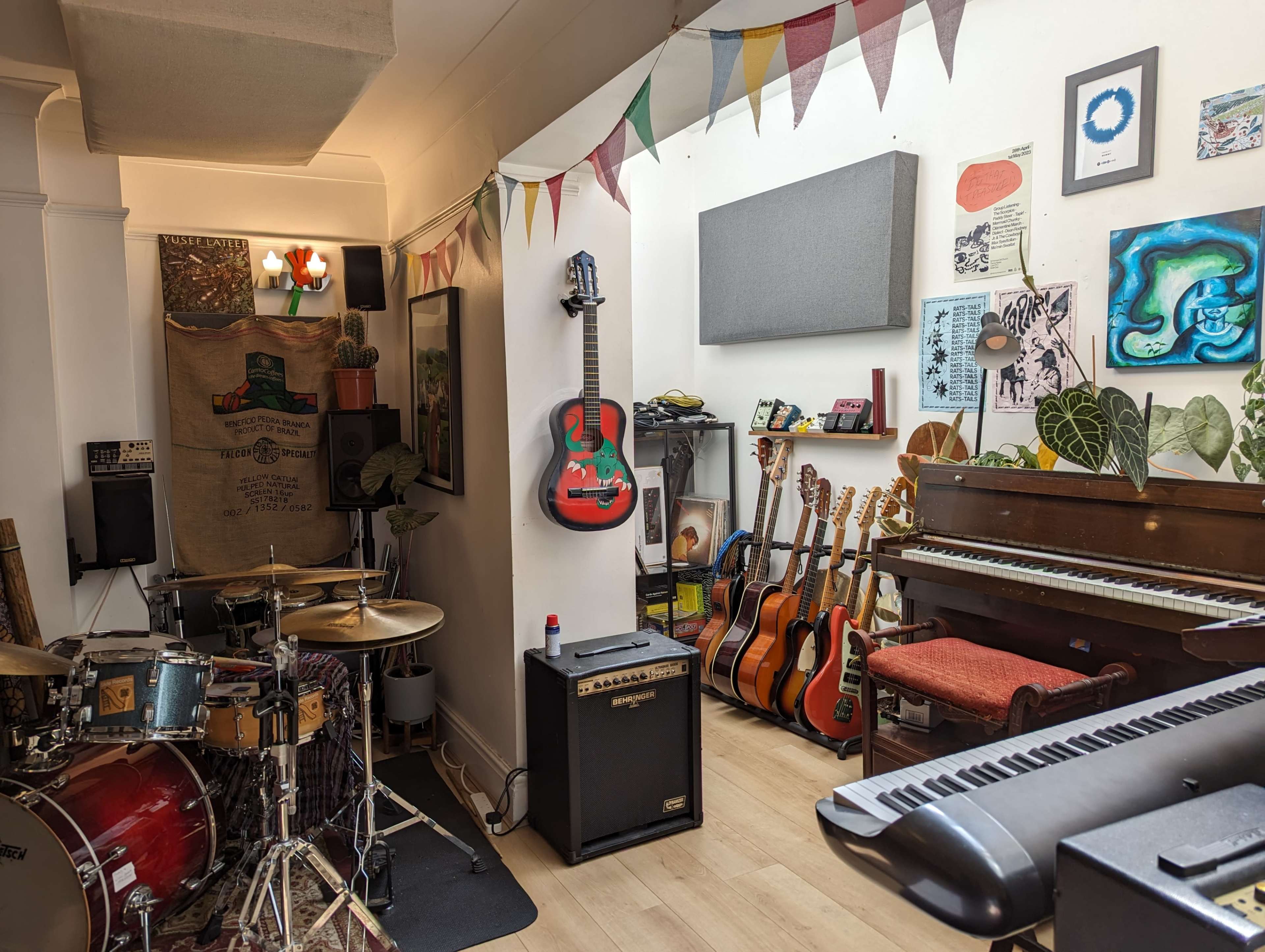 The image shows a music studio filled with various instruments, including a drum set, guitars, a piano, and decorative artwork on the walls.