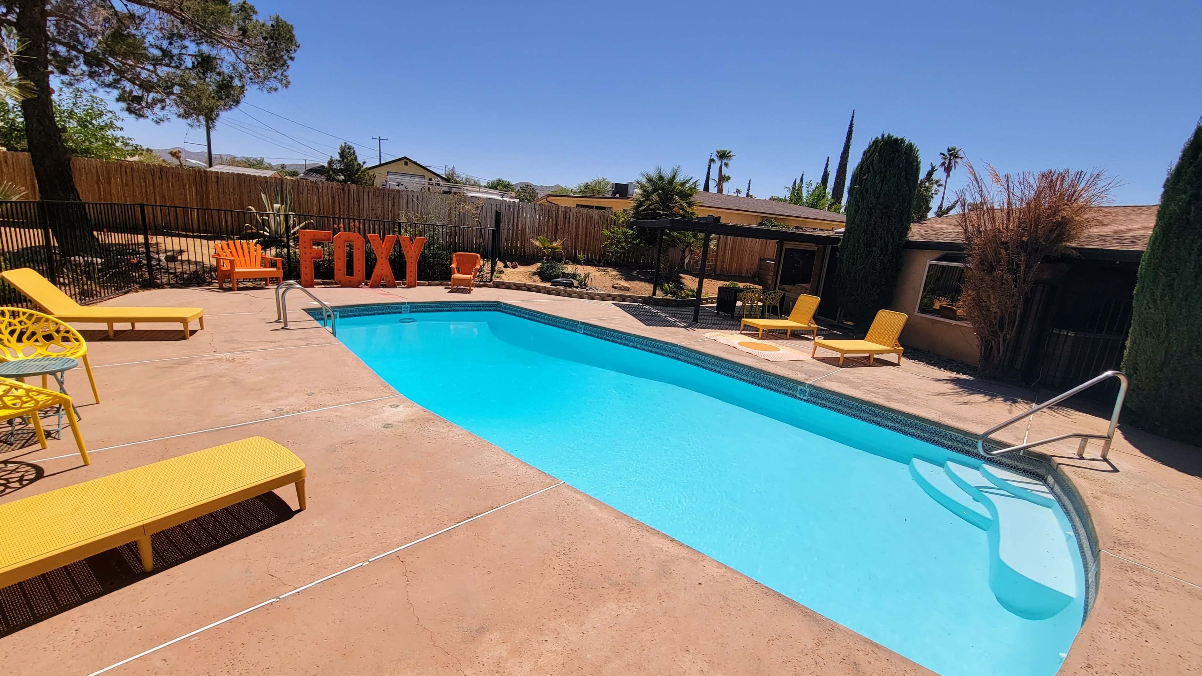 A swimming pool surrounded by yellow lounge chairs, with a large red sign reading "FOXY" in the background.