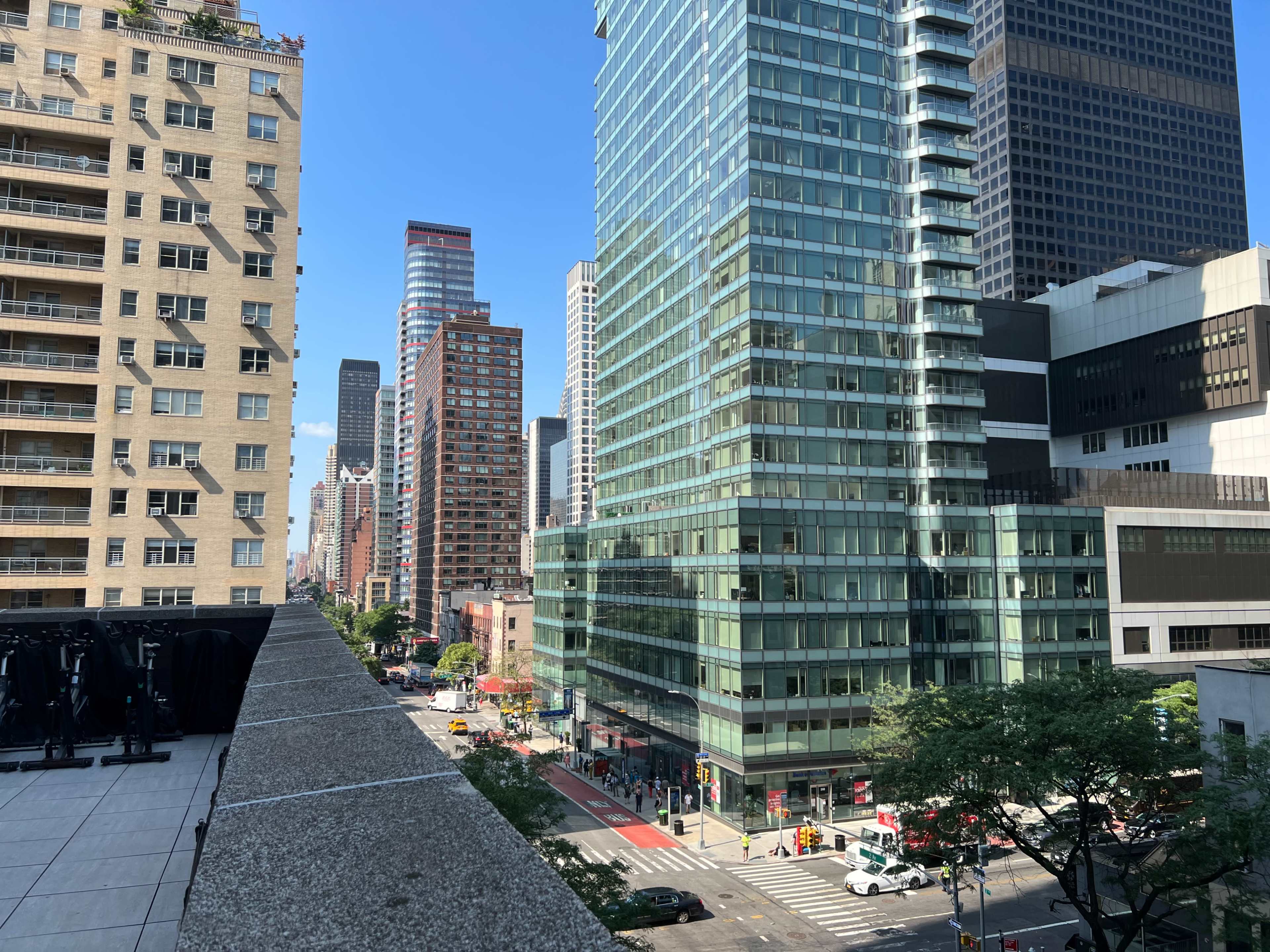The image shows a cityscape featuring tall glass buildings and a busy intersection in an urban setting under a clear blue sky.
