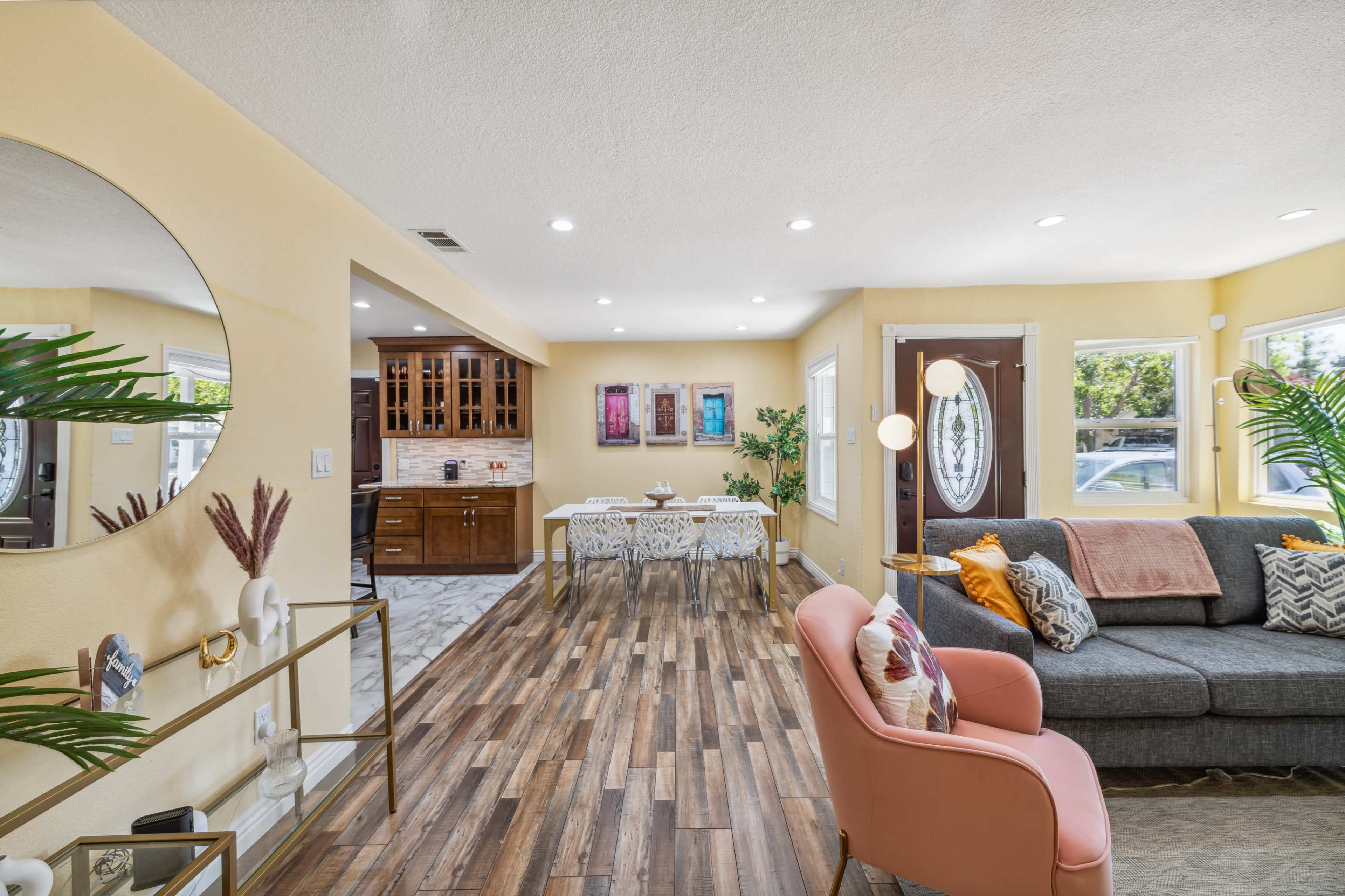 A modern living room with a gray sofa, a pink chair, a dining area with a table, and a kitchen in an open-concept layout.