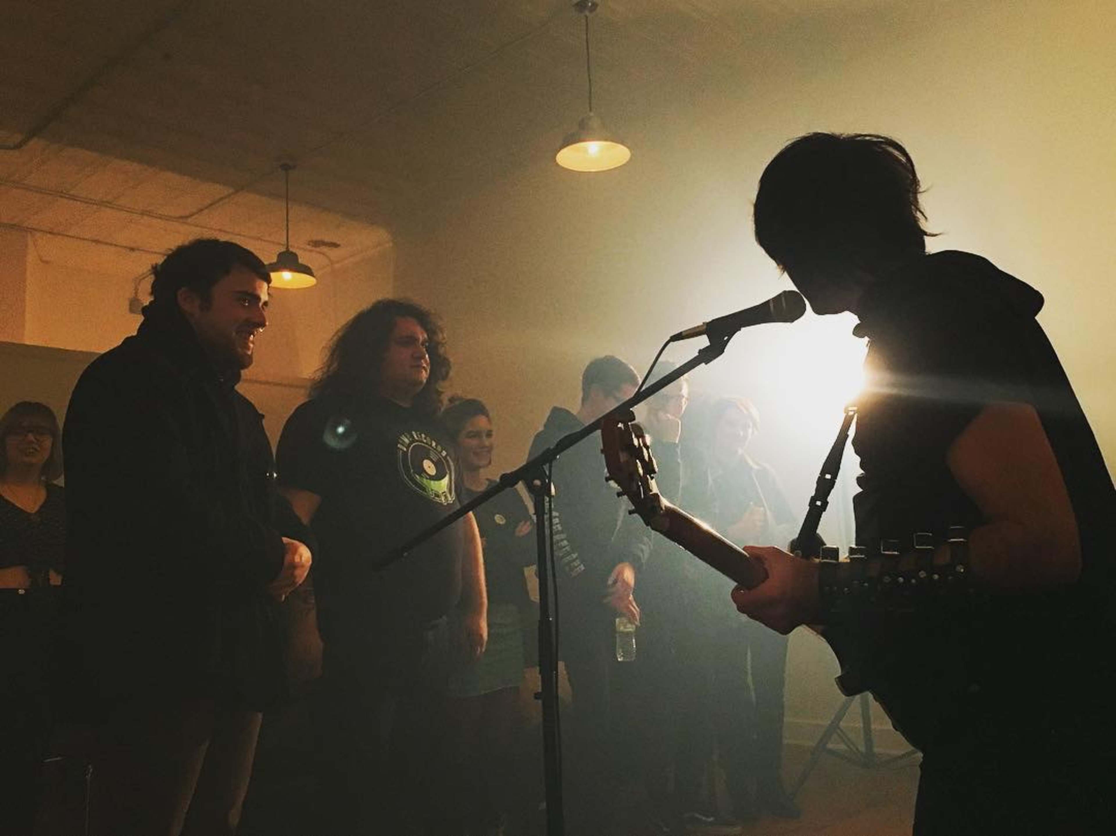 A musician performs on stage while an audience watches intently in a dimly lit room.