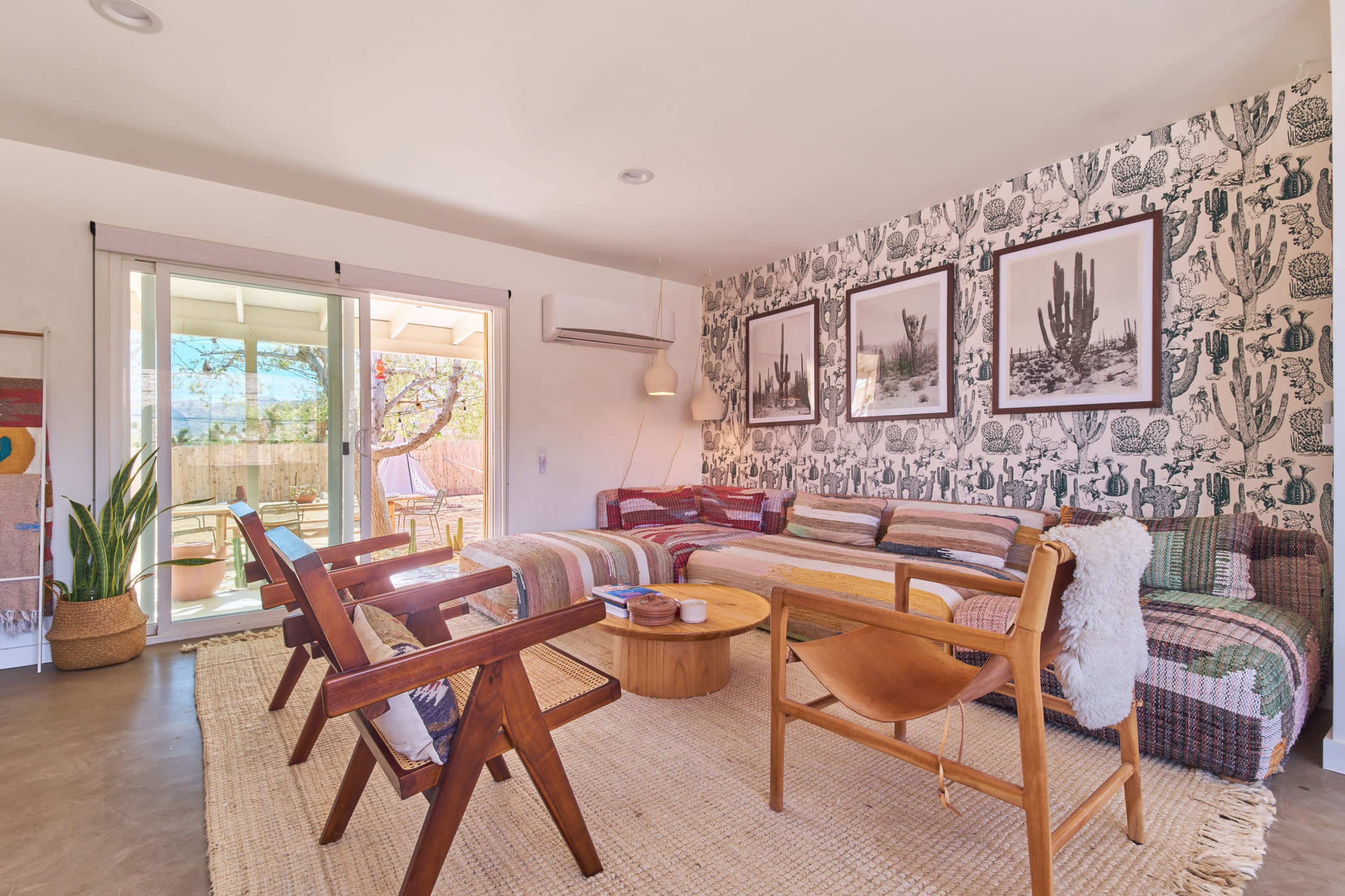 A stylish living room with a patterned wall, a round wooden coffee table, and various seating arrangements, including two wooden chairs and a sofa adorned with cushions.