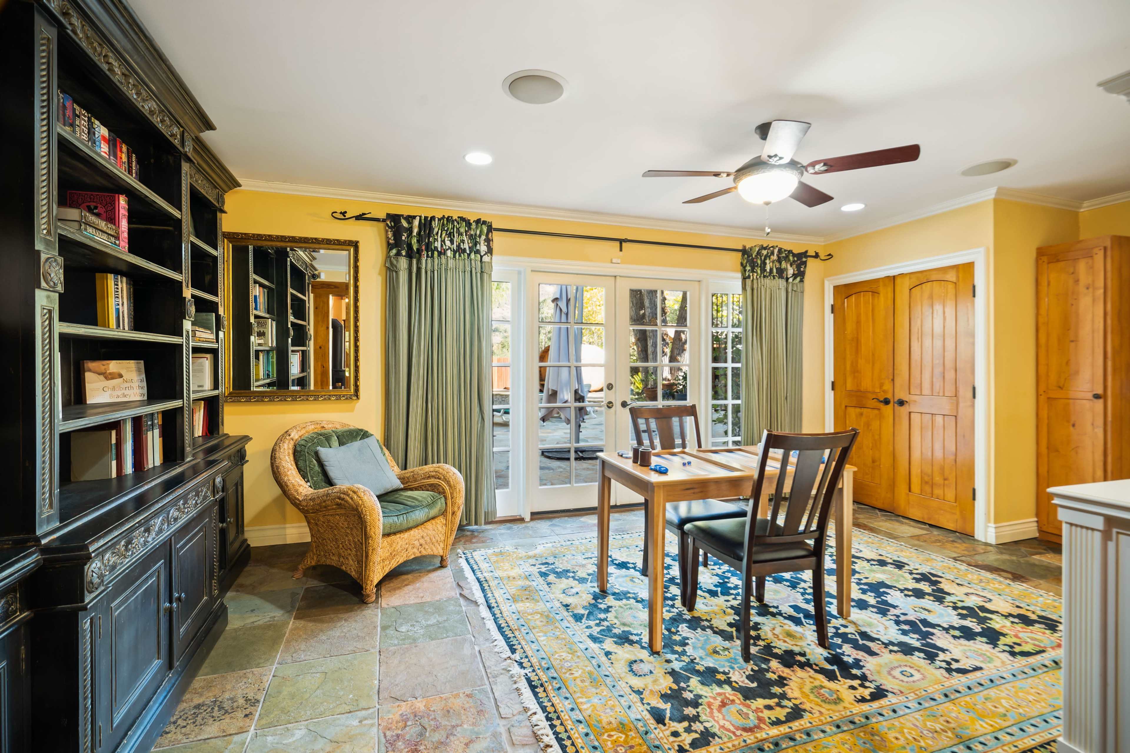 A cozy room features a table and chairs, a bookshelf, and a door leading to an outdoor area.