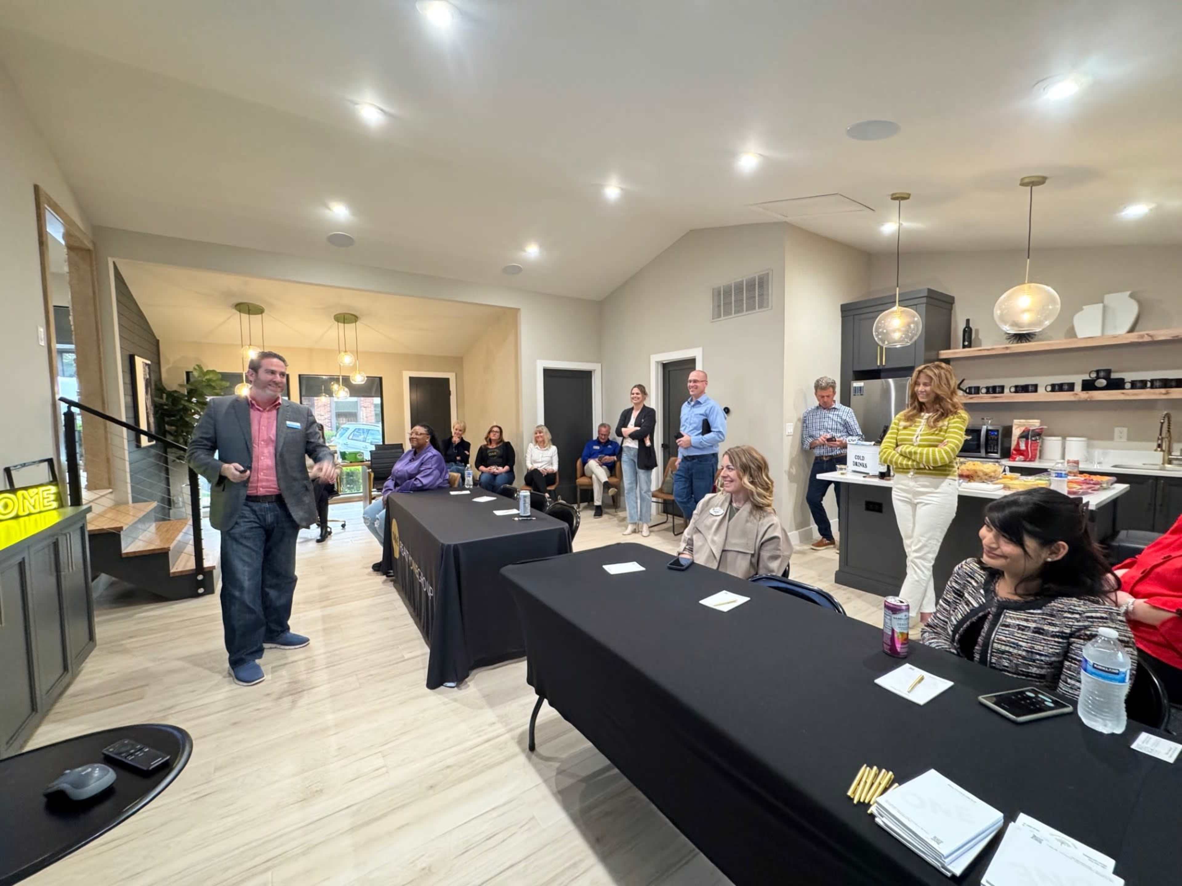 A speaker presents to an audience seated at tables in a modern meeting space.