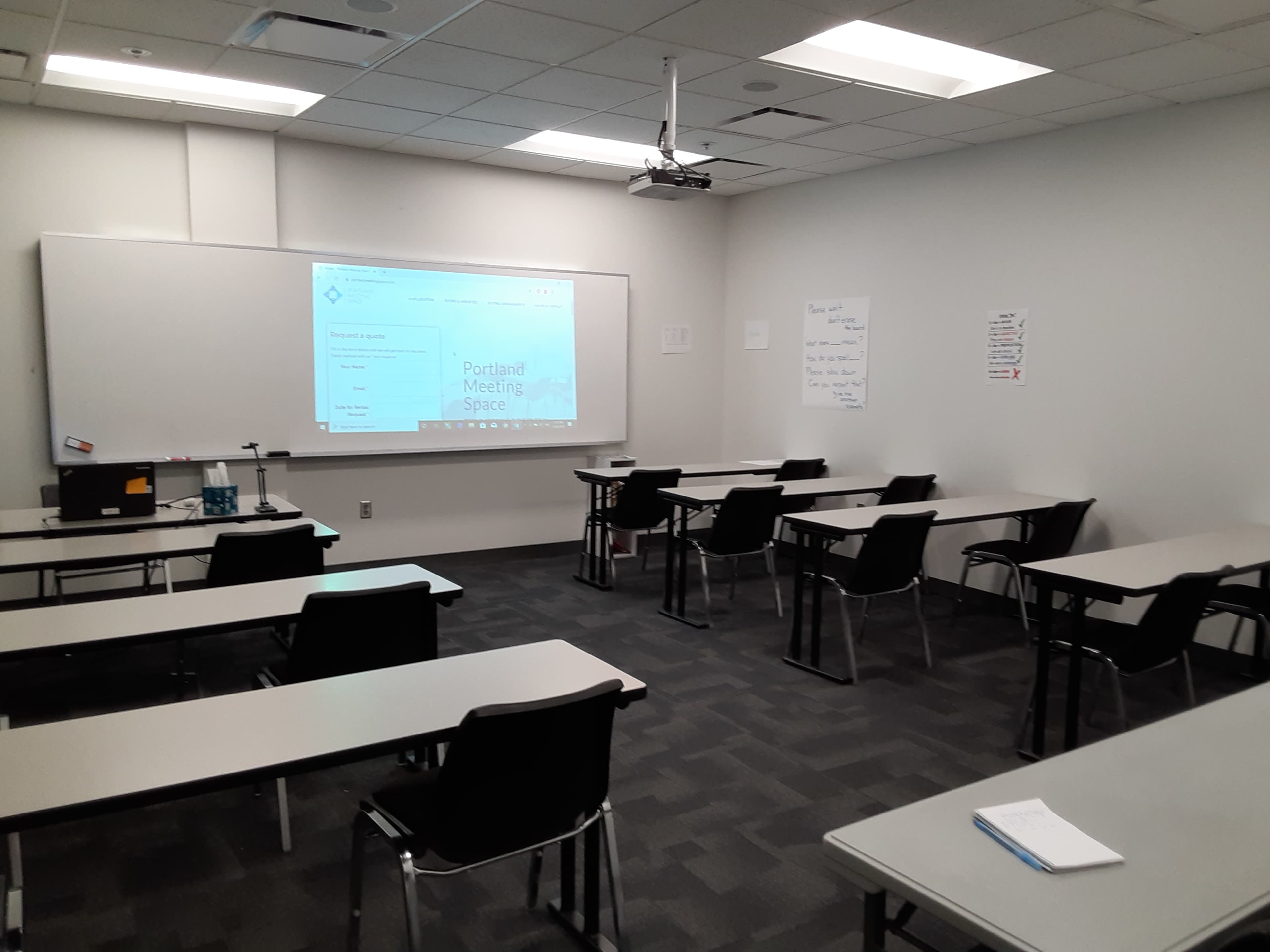 A conference room is configured with rows of tables and chairs, featuring a projector screen displaying a meeting agenda.